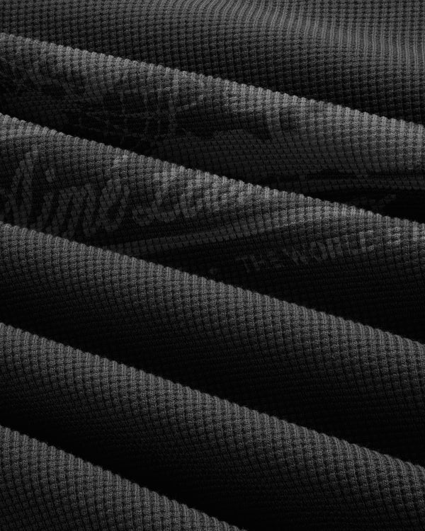 Close-up of Long-Sleeve Unisphere Waffle Thermal, dark ribbed fabric folded in parallel diagonal lines.