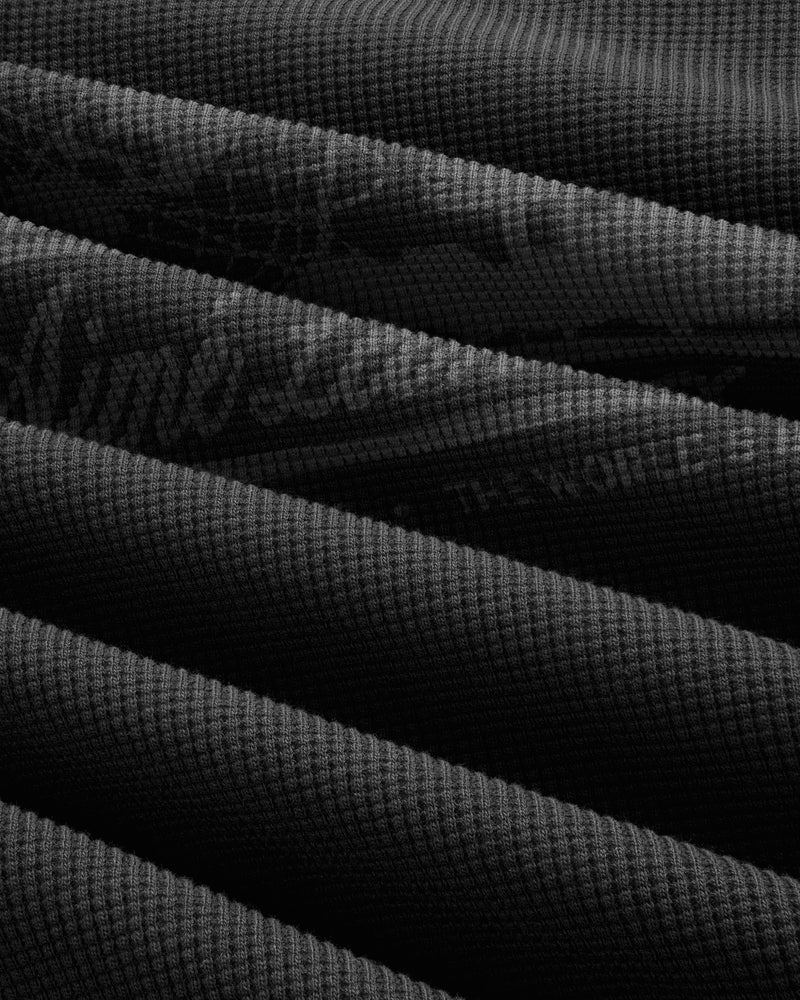 Close-up of Long-Sleeve Unisphere Waffle Thermal, dark ribbed fabric folded in parallel diagonal lines.