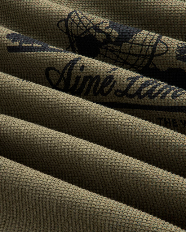 Close-up of olive green Long-Sleeve Unisphere Waffle Thermal with black printed text and graphic details.
