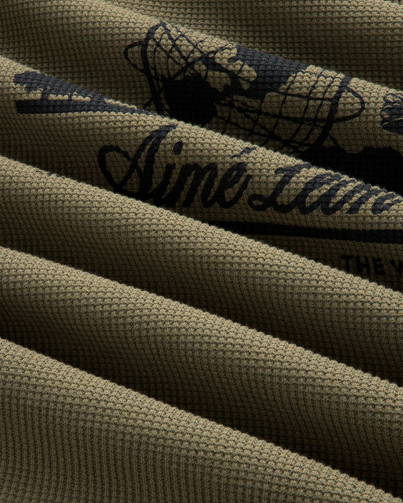 Close-up of olive green Long-Sleeve Unisphere Waffle Thermal with black printed text and graphic details.