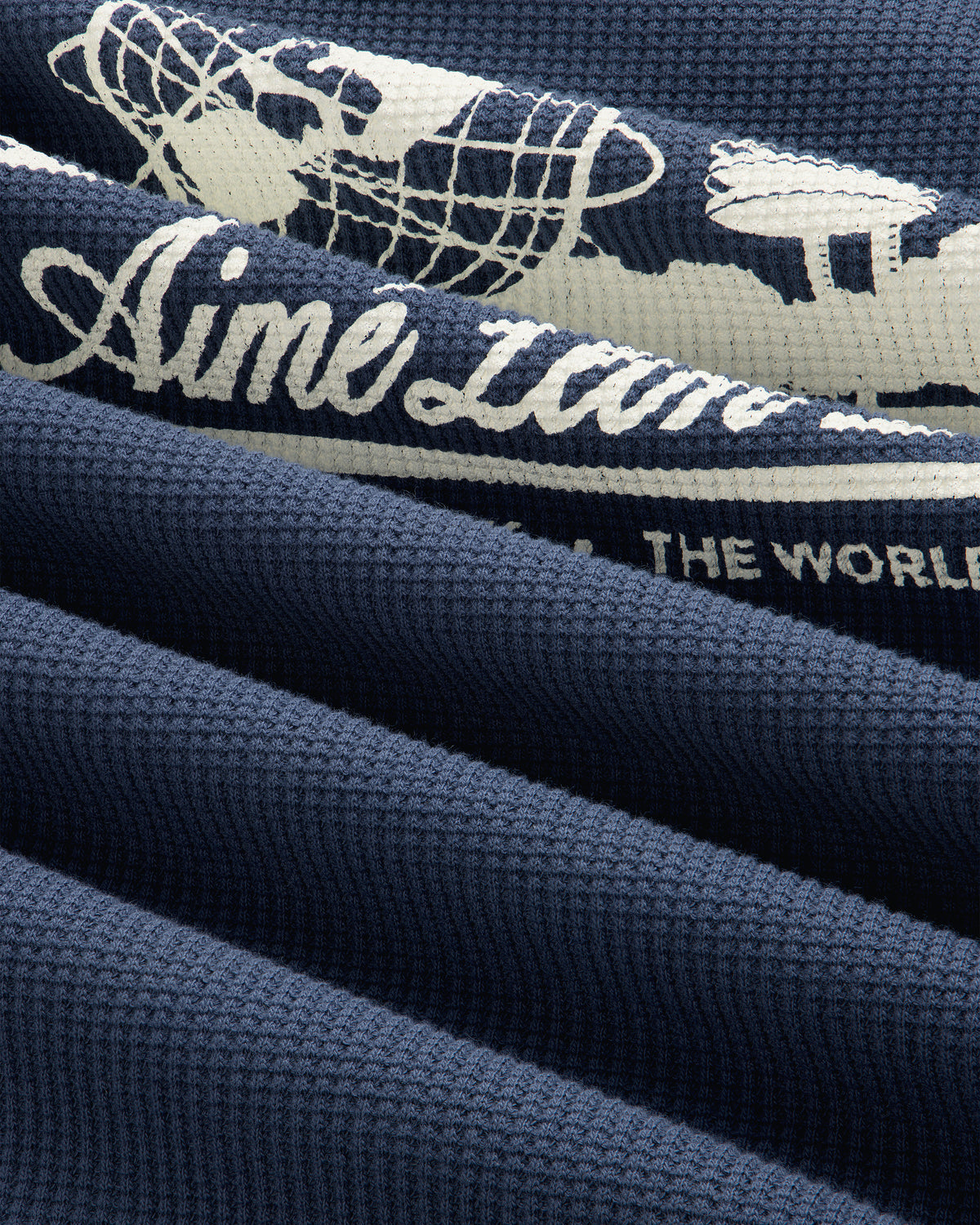 Navy Unisphere Waffle Thermal with white vintage airplane, globe graphic, and partial “Aime ... the World” text.