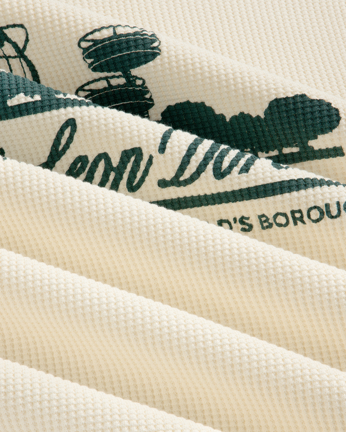 Close-up of Long-Sleeve Unisphere Waffle Thermal, cream-colored with green print visible between fabric folds.
