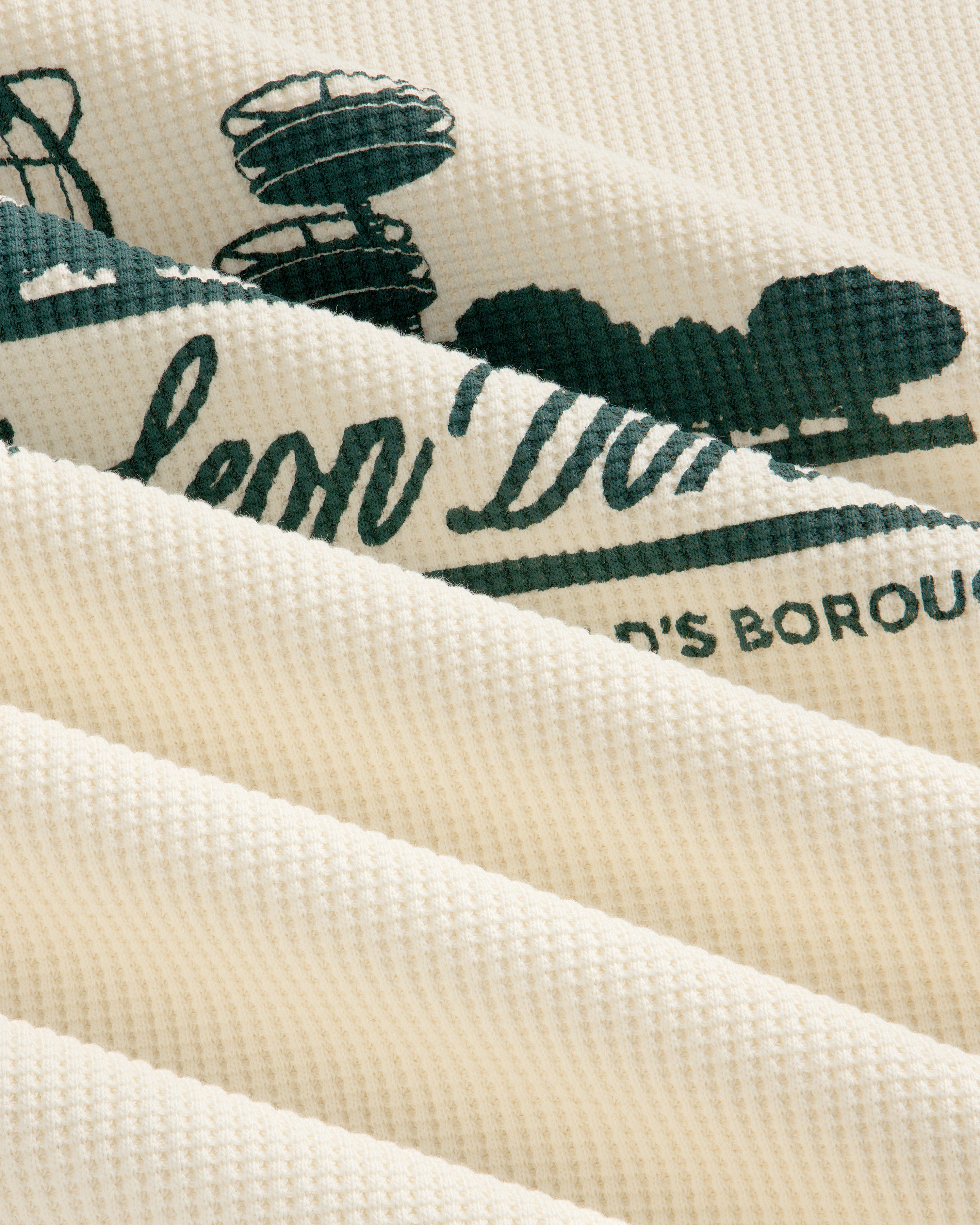 Close-up of Long-Sleeve Unisphere Waffle Thermal, cream-colored with green print visible between fabric folds.