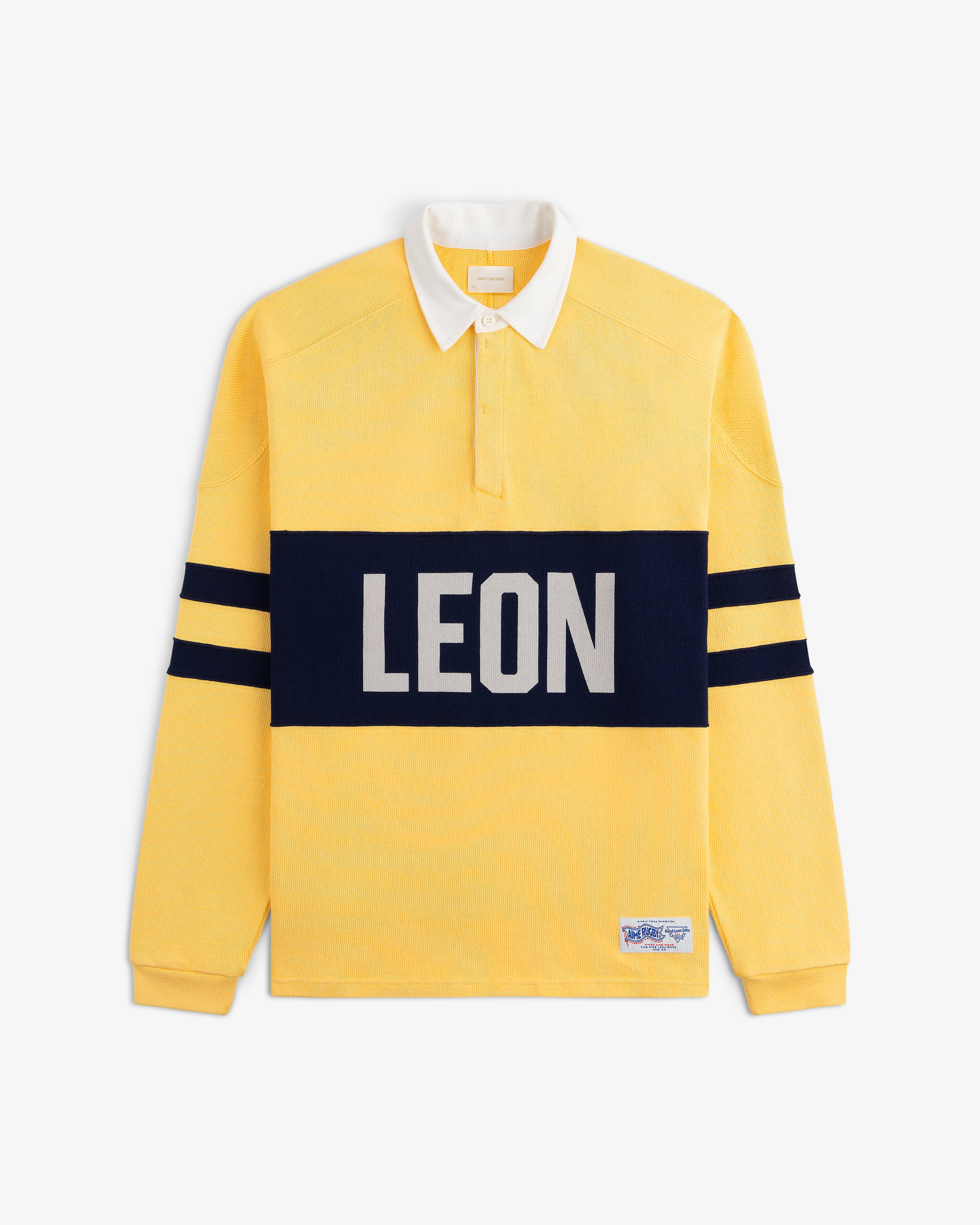 Leon Dore Collegiate Rugby: yellow long-sleeve shirt with white collar, navy stripes, and bold LEON across the chest.