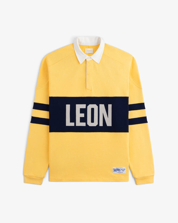 Leon Dore Collegiate Rugby: yellow long-sleeve shirt with white collar, navy stripes, and bold LEON across the chest.