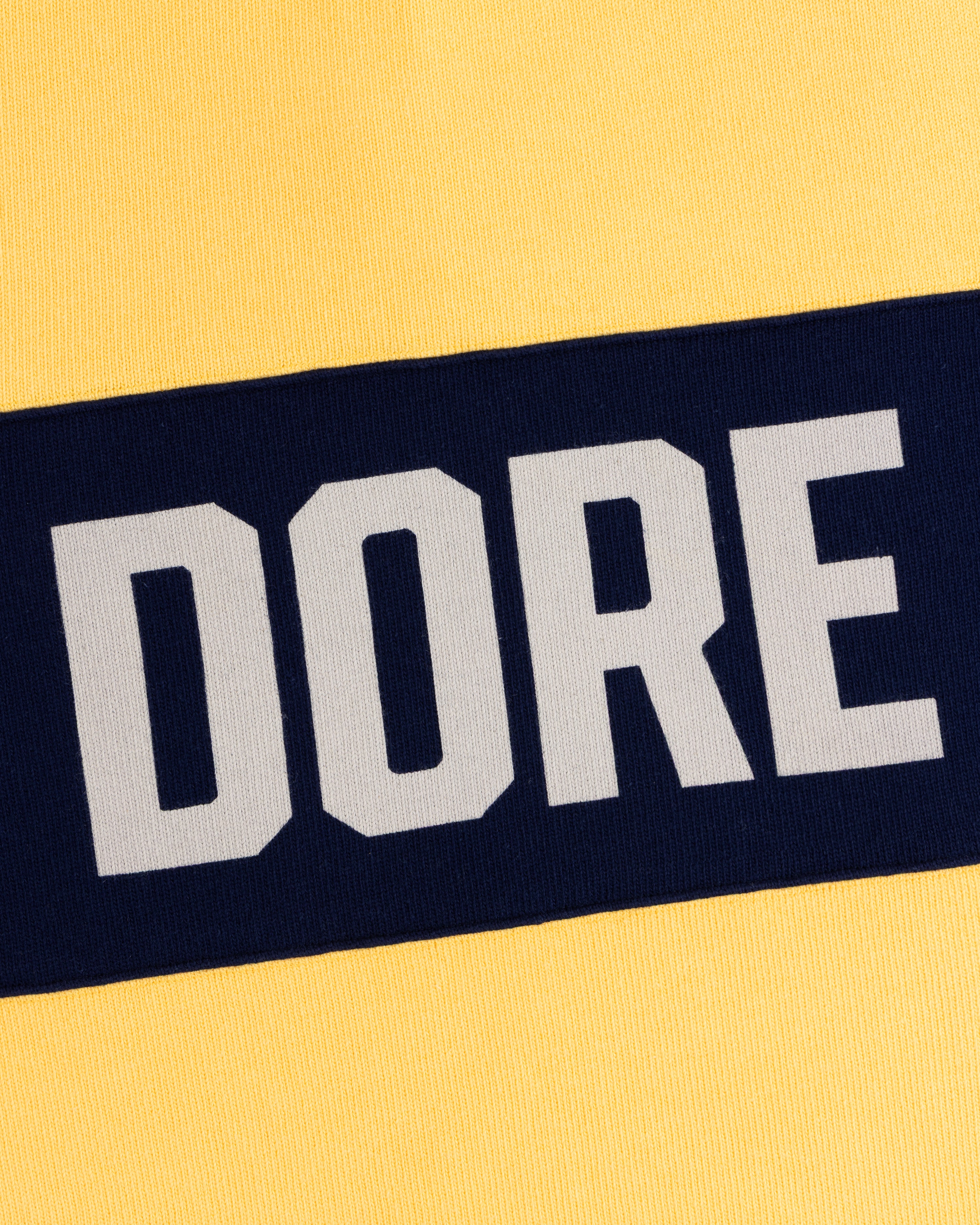 Yellow Leon Dore Collegiate Rugby with a navy stripe and DORE in bold white letters.