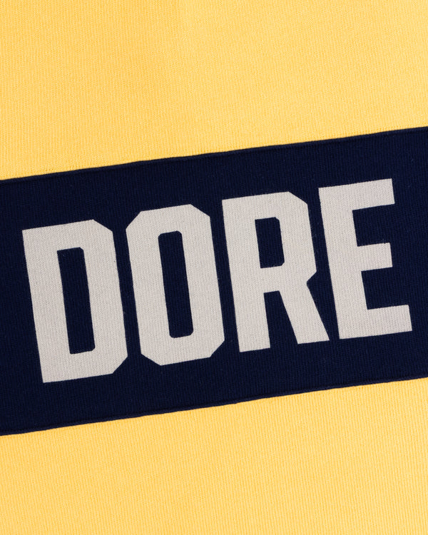 Yellow Leon Dore Collegiate Rugby with a navy stripe and DORE in bold white letters.