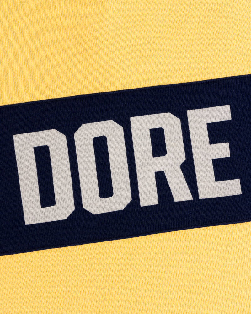 Yellow Leon Dore Collegiate Rugby with a navy stripe and DORE in bold white letters.