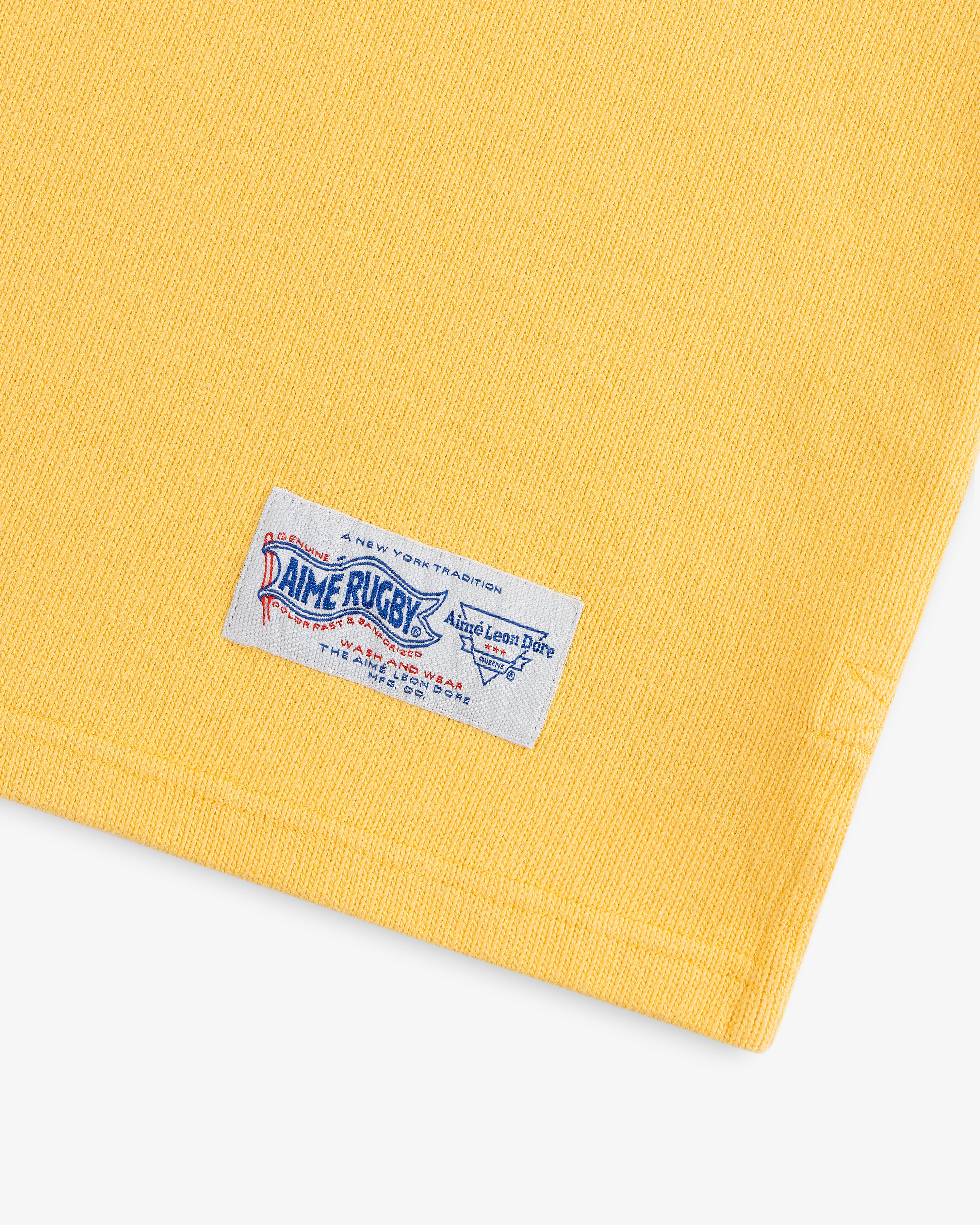 Yellow Leon Dore Collegiate Rugby with a white “Rugby” tag near the hem, displayed on a white background.