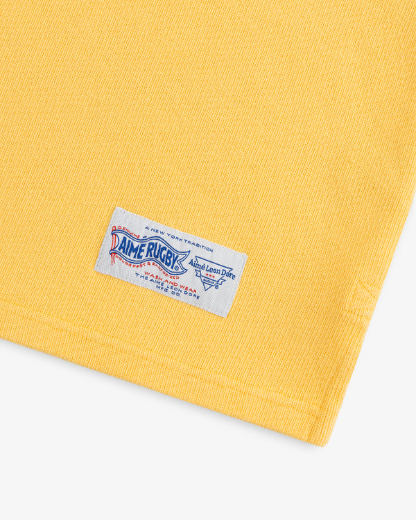 Yellow Leon Dore Collegiate Rugby with a white “Rugby” tag near the hem, displayed on a white background.