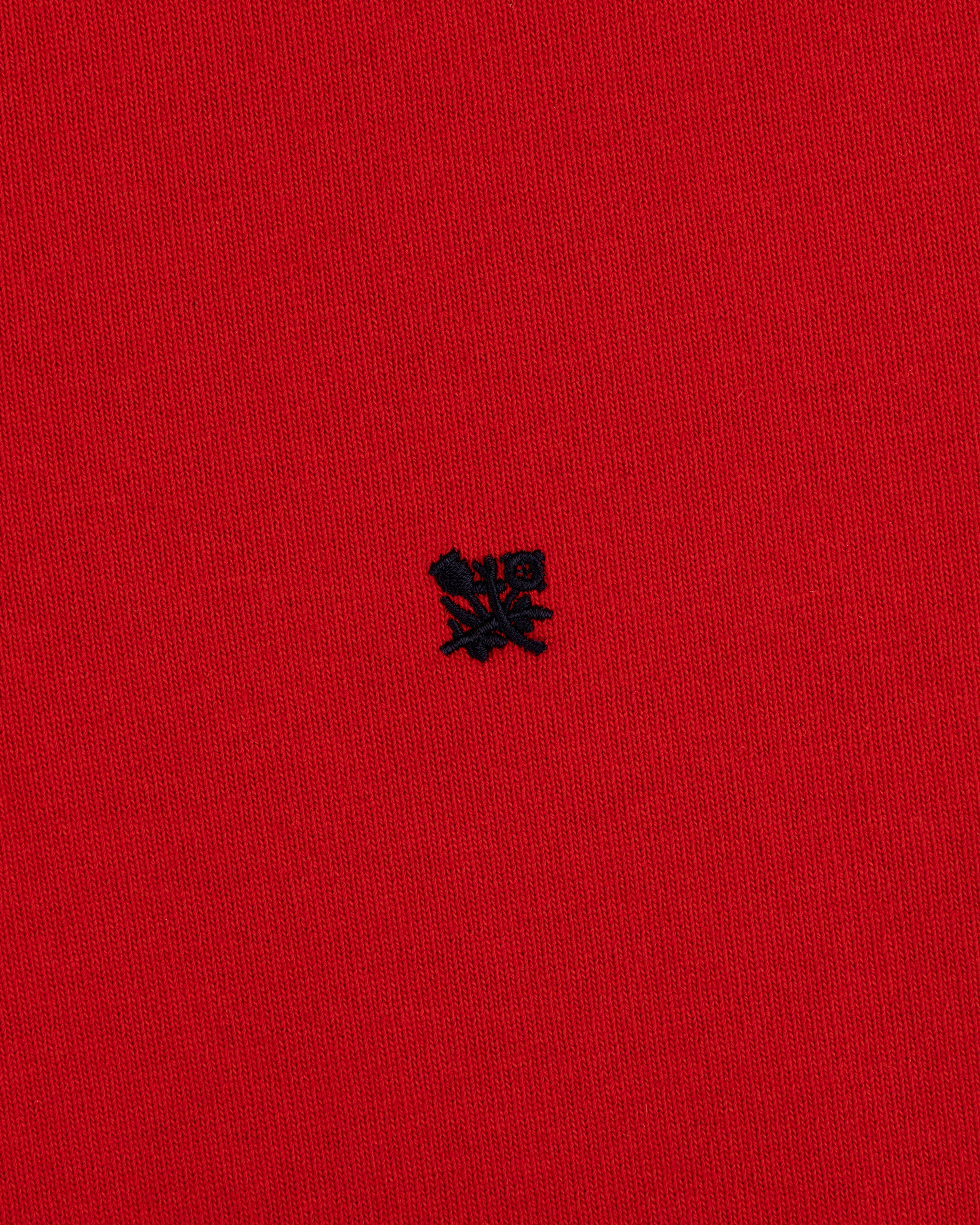 A small black embroidered Crest Rugby logo on bright red textured fabric.