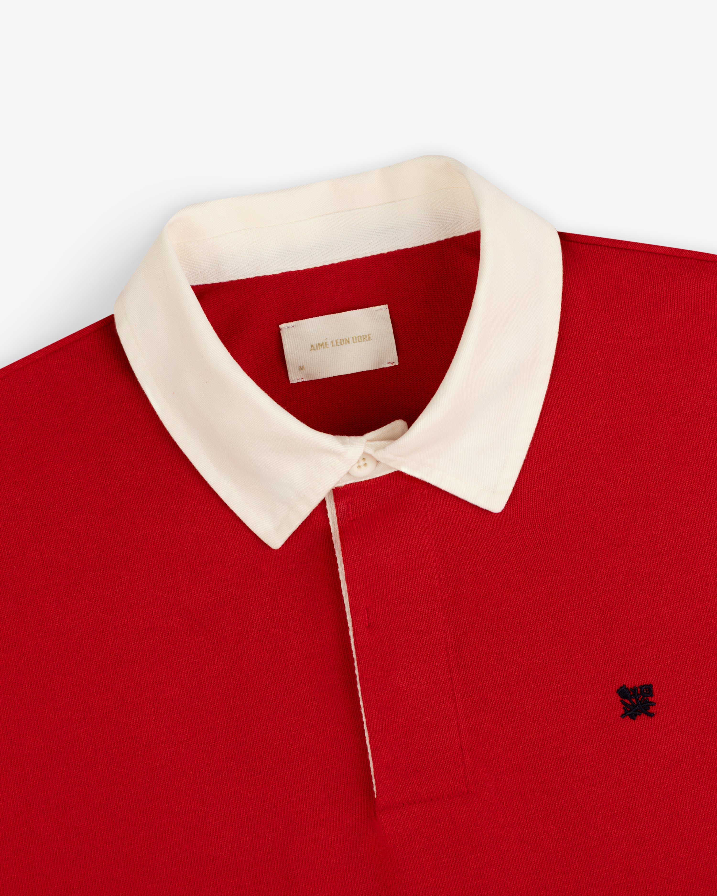 Crest Rugby: Red polo with white collar, white buttons, and small black logo embroidered on chest.