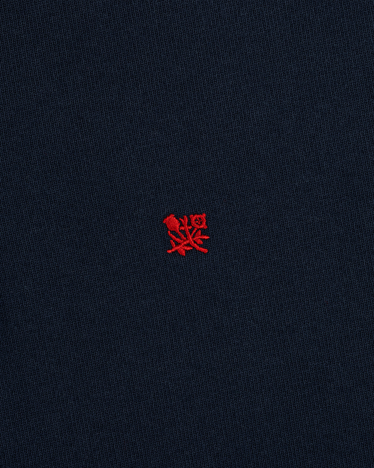 The Crest Rugby features navy blue fabric with a small red embroidered emblem centered on the front.