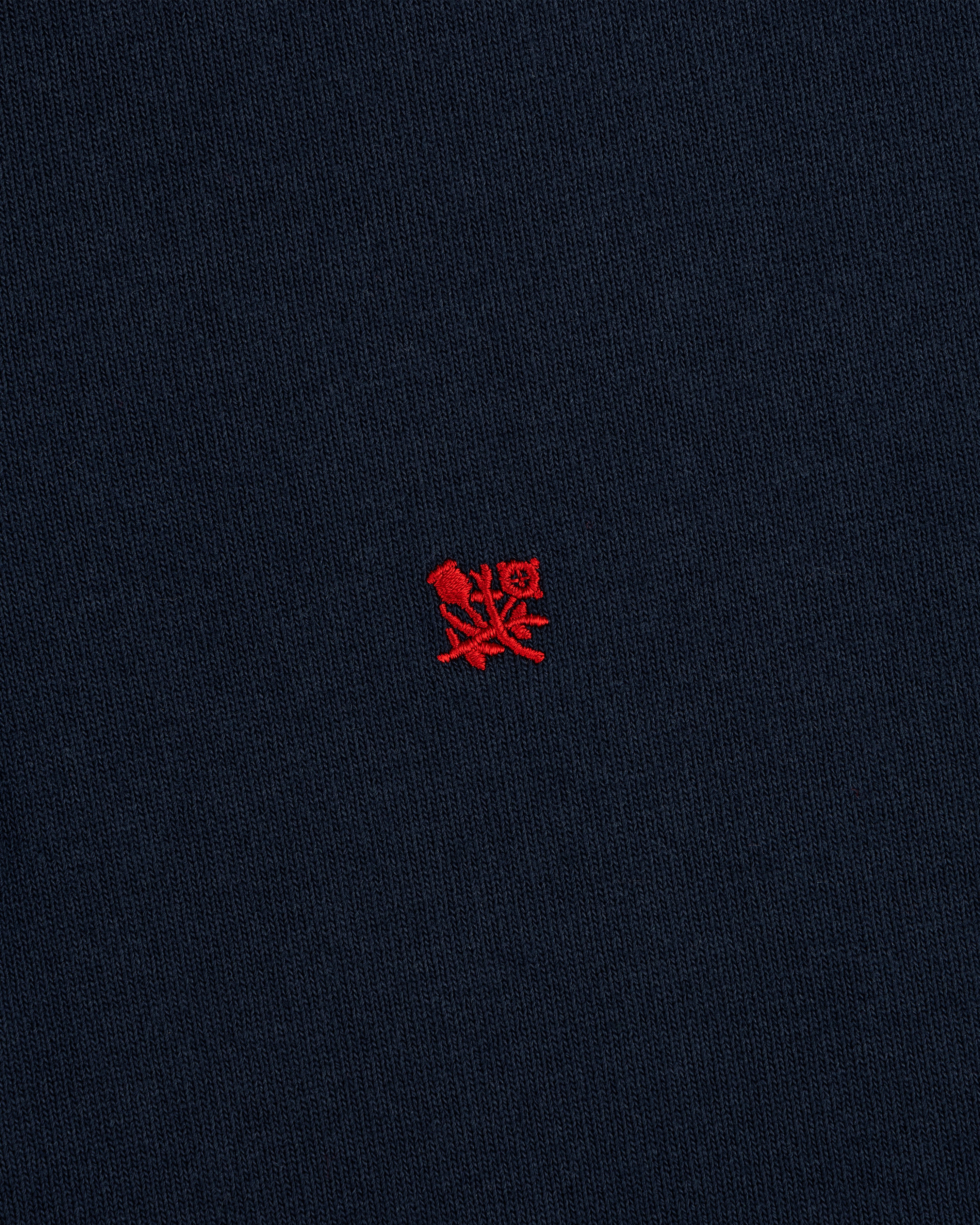 The Crest Rugby features navy blue fabric with a small red embroidered emblem centered on the front.