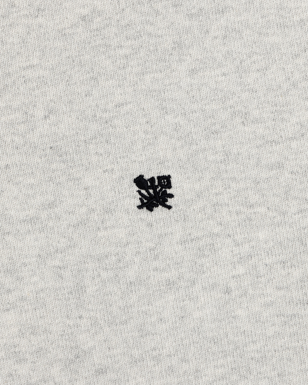 A small black crest is embroidered on the center of the Crest Rugby’s light gray fabric background.