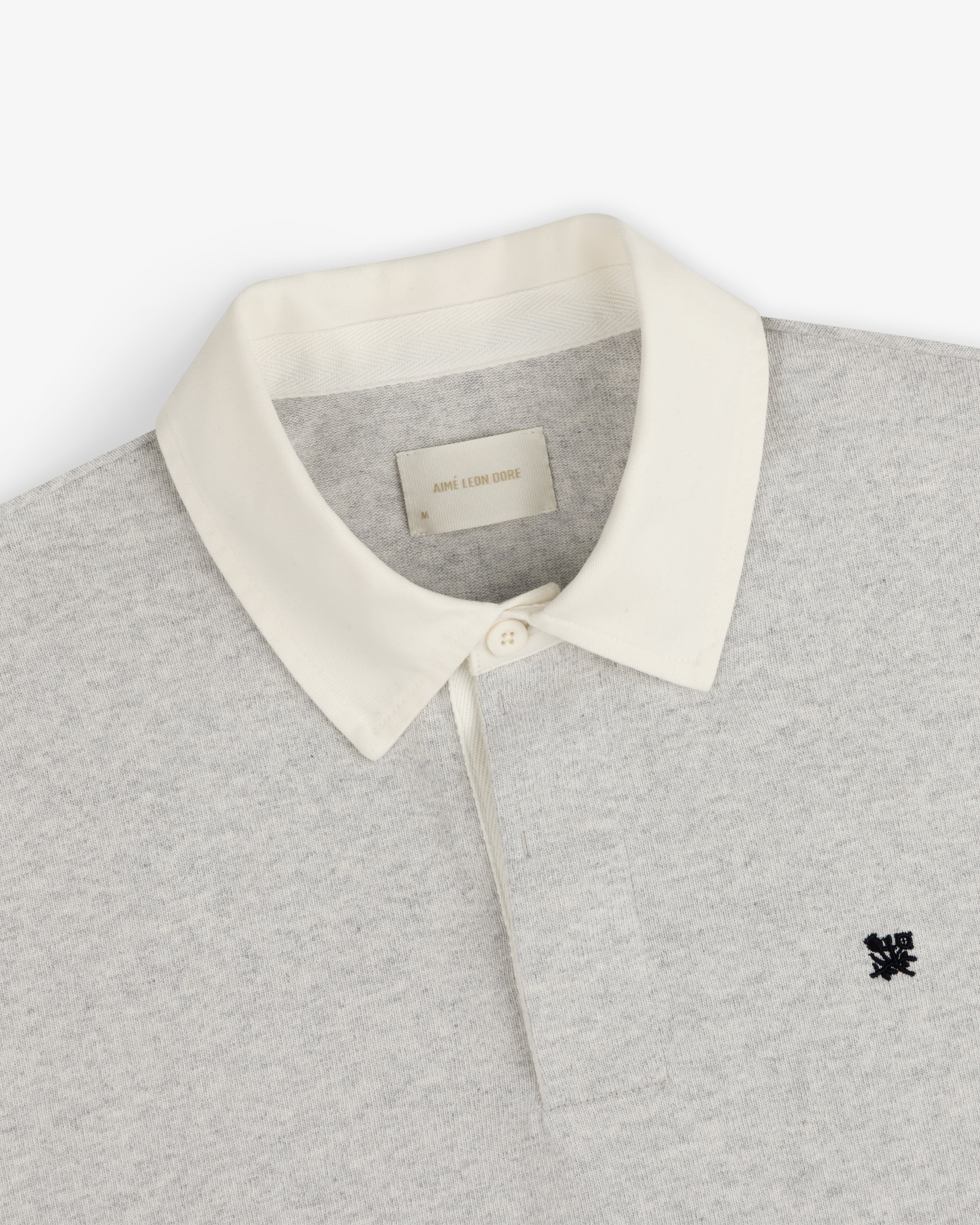 Crest Rugby: Light grey polo with white collar, black chest logo, and inside white neck label.