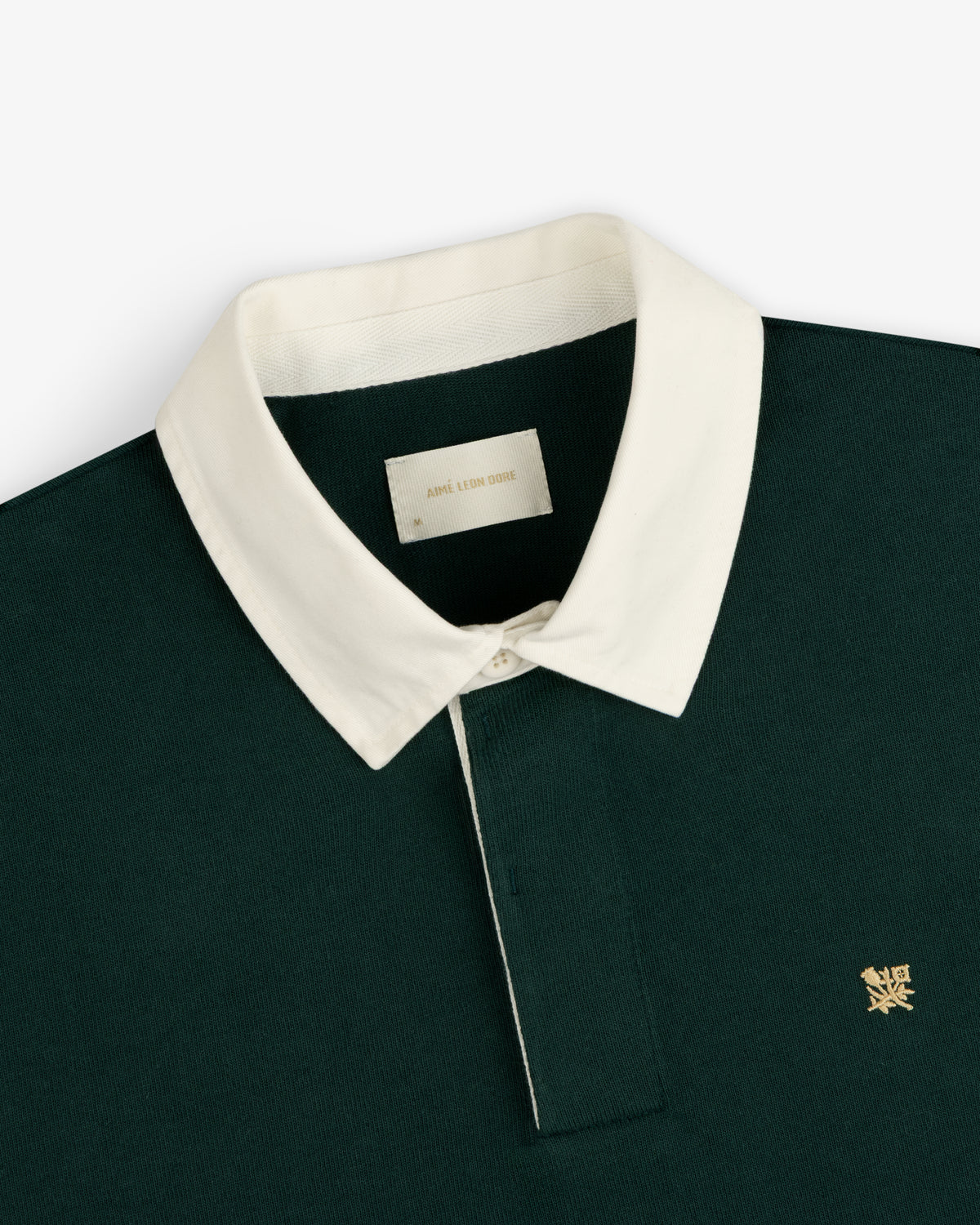 Crest Rugby: Dark green shirt with white collar and small gold logo embroidered on the left chest.