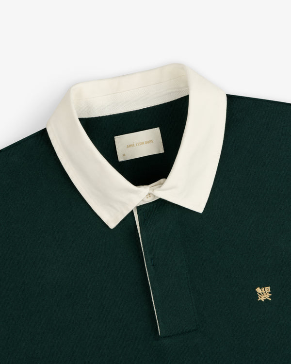Crest Rugby: Dark green shirt with white collar and small gold logo embroidered on the left chest.
