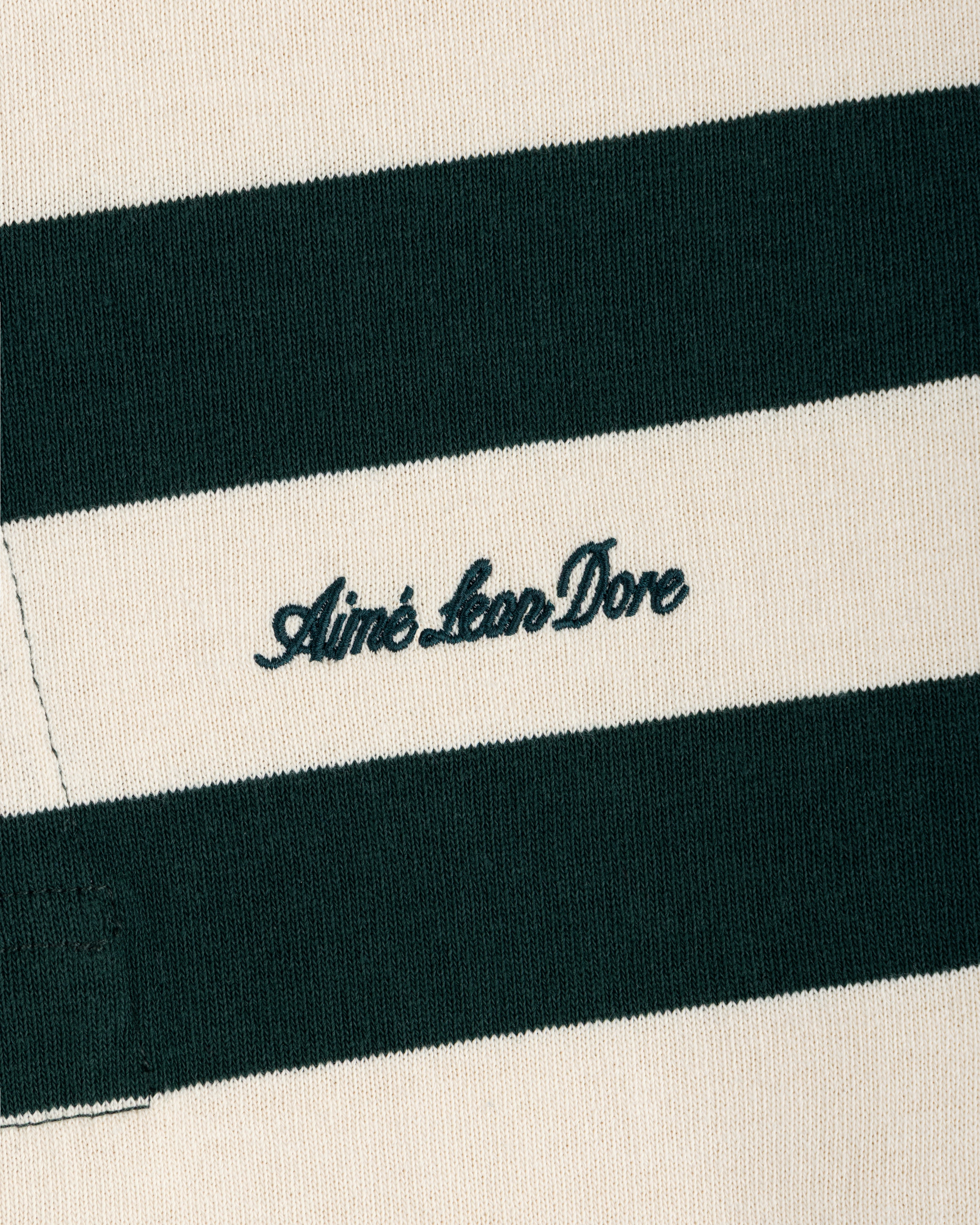 Striped Script Rugby in cream and dark green striped fabric with Aimé Leon Dore embroidered in dark green script.