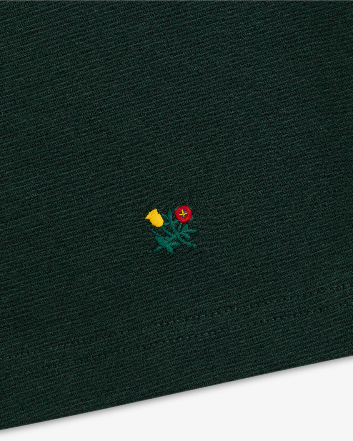 Heavyweight Crest Mockneck Tee in dark green fabric with a small embroidered emblem of a red and yellow flower.