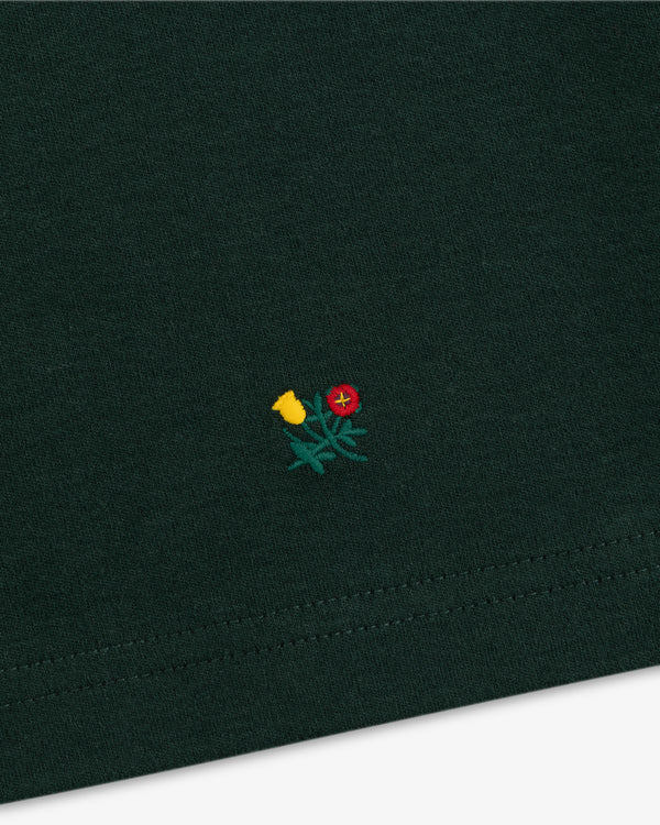 Heavyweight Crest Mockneck Tee in dark green fabric with a small embroidered emblem of a red and yellow flower.