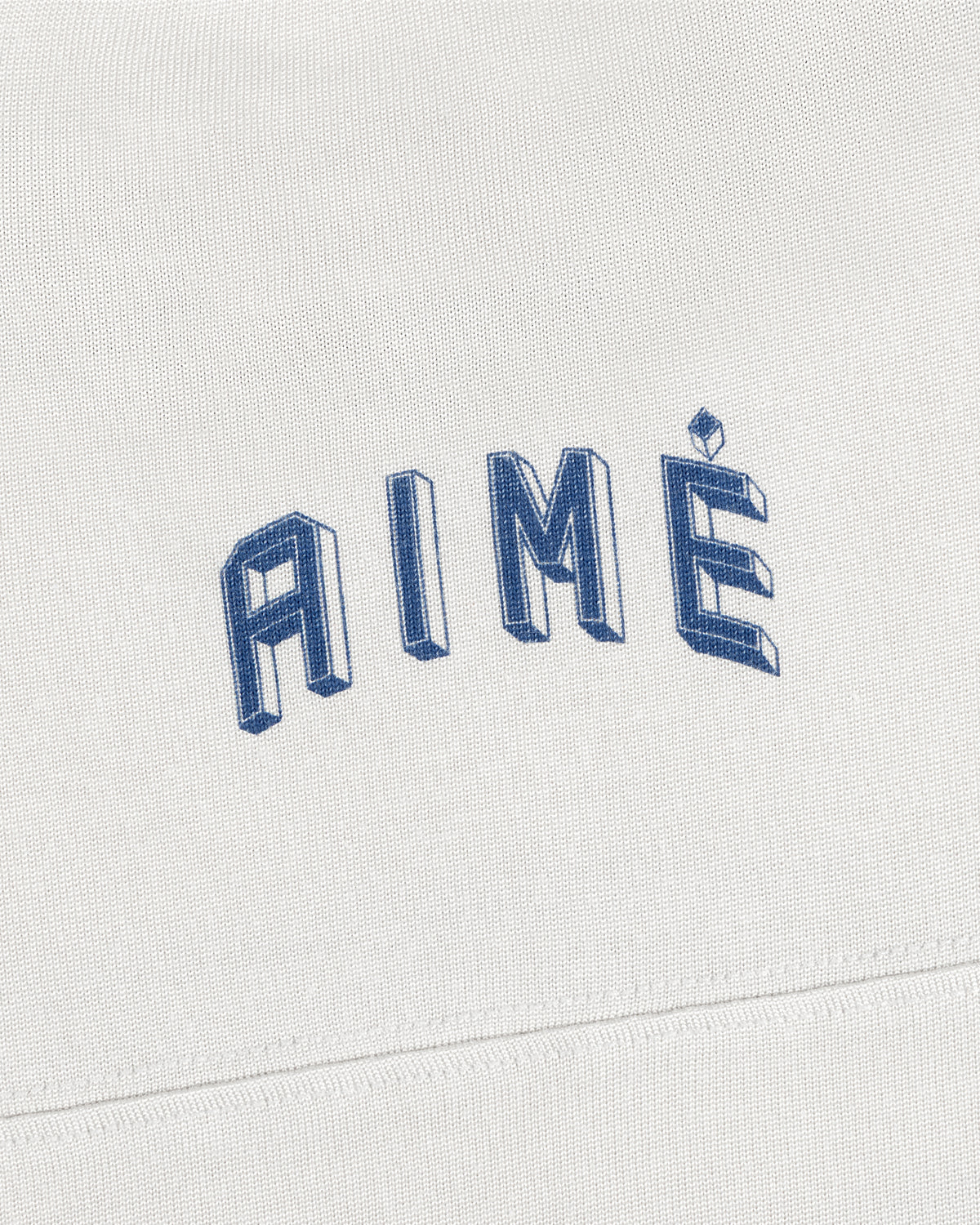 A white Football Ringer Tee with AIMÉ embroidered in arched, blue 3D-style block lettering.