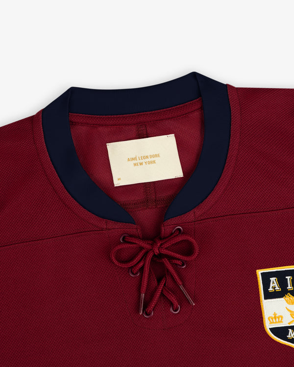Team Aimé Hockey Jersey in maroon with a lace-up collar, navy blue trim, and a brand label at the neckline.