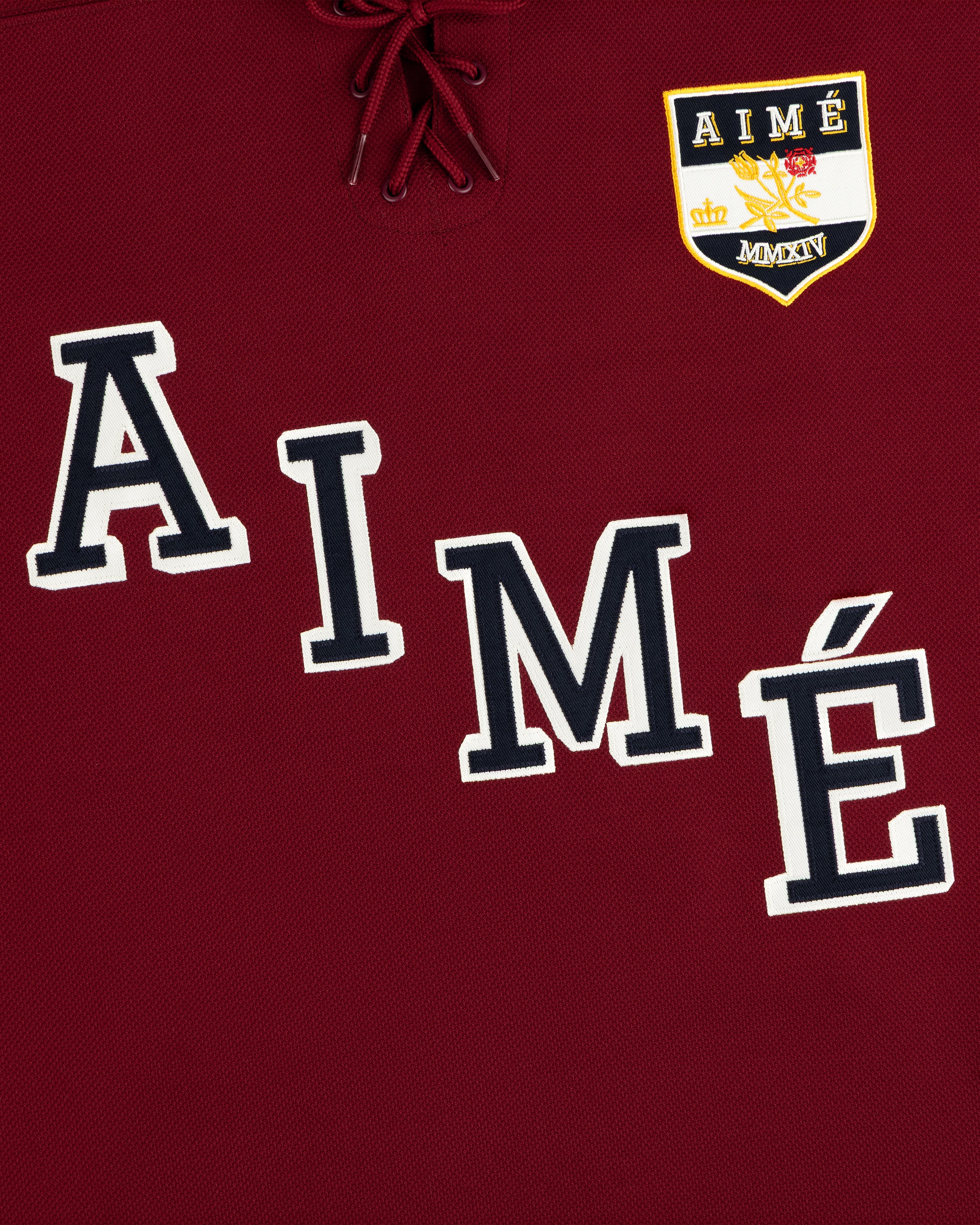 Team Aimé Hockey Jersey: maroon with a lace-up collar, varsity-style AIMÉ lettering, and a crown and floral crest.