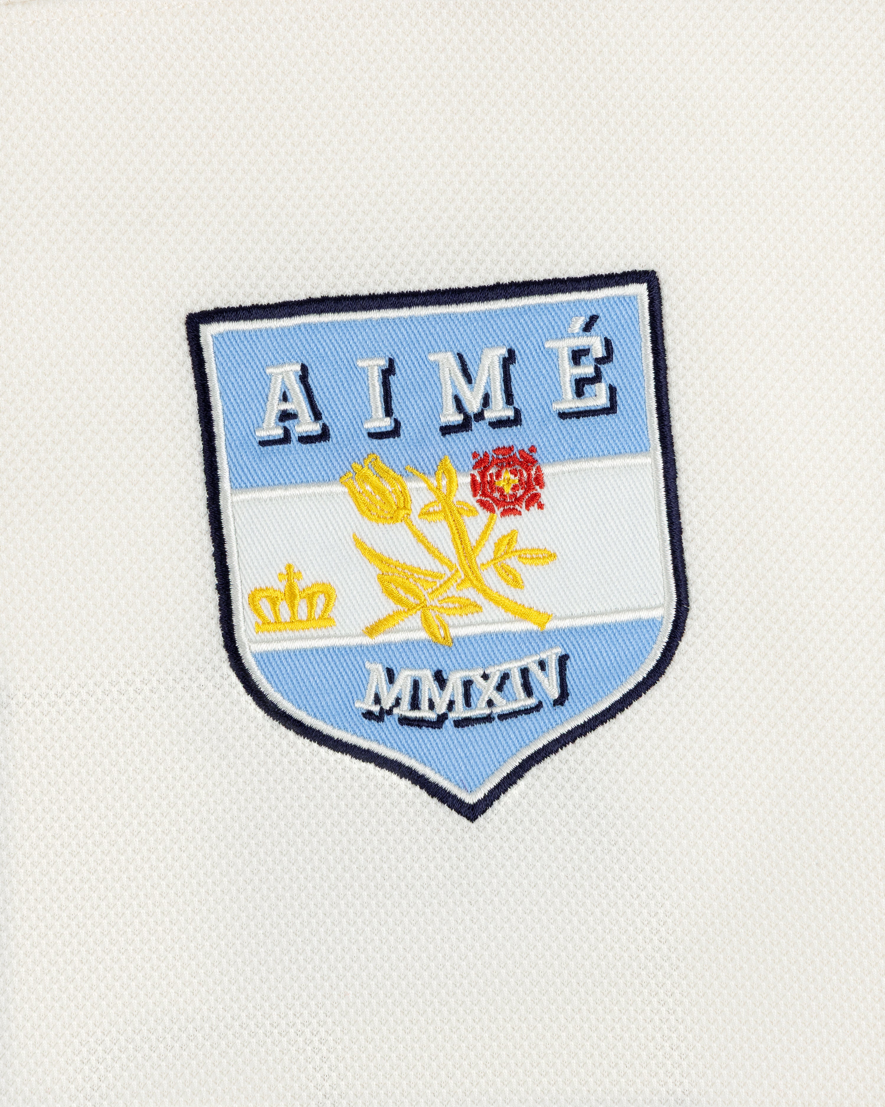 Team Aimé Hockey Jersey featuring an embroidered shield patch on white fabric with a flower, crown, AIMÉ, and MMXIV.