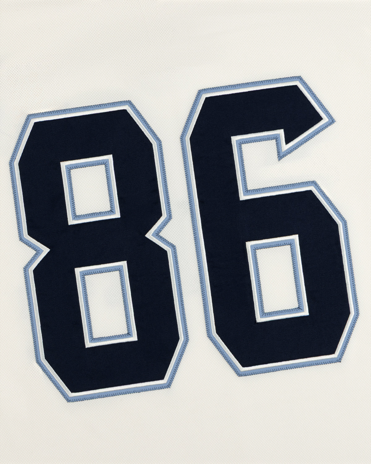 Dark blue athletic number 86 with light blue and white stitched trim on a white Team Aimé Hockey Jersey.