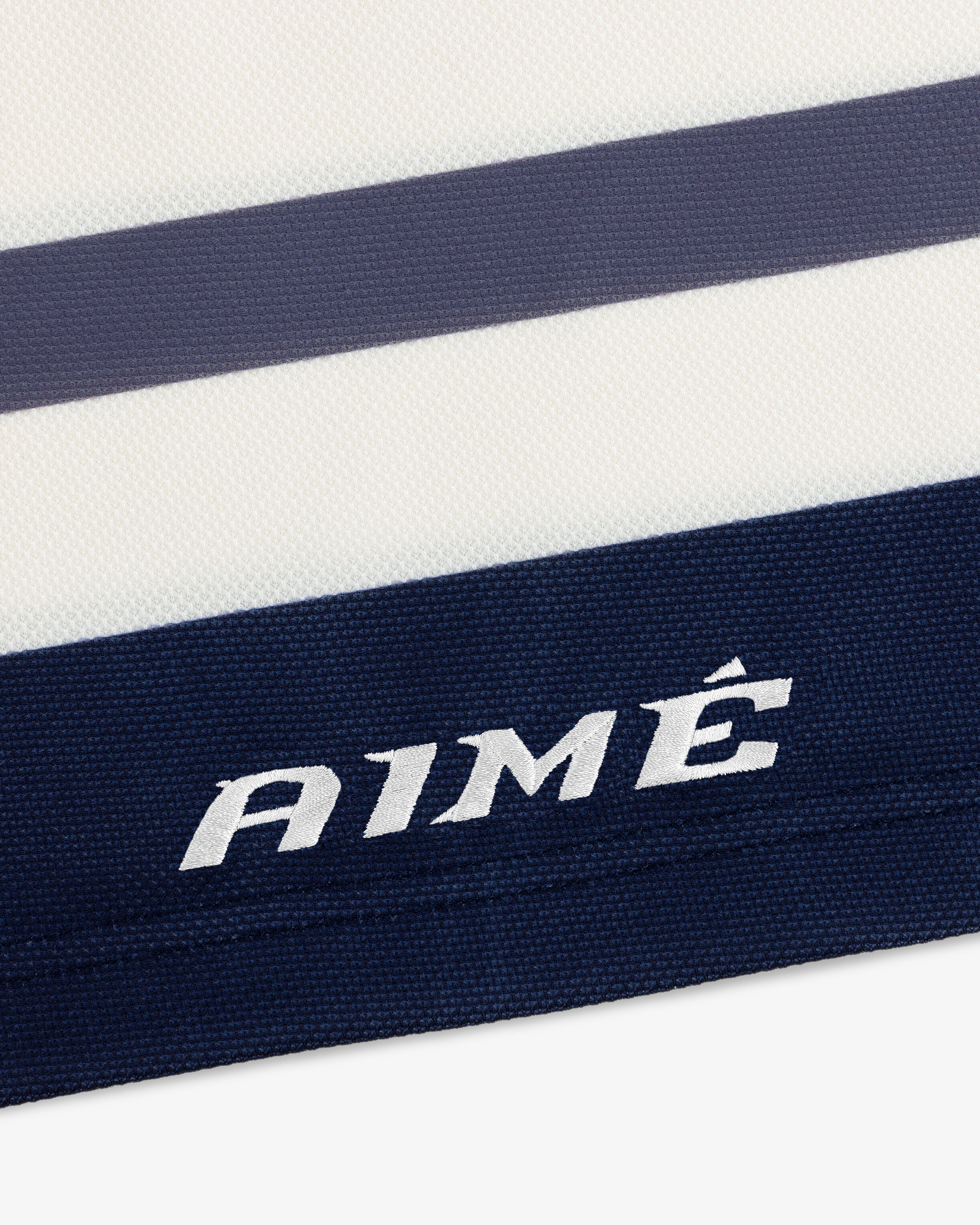 Close-up of a white Team Aimé Hockey Jersey with navy and grey horizontal stripes and AIMÉ embroidered in white.