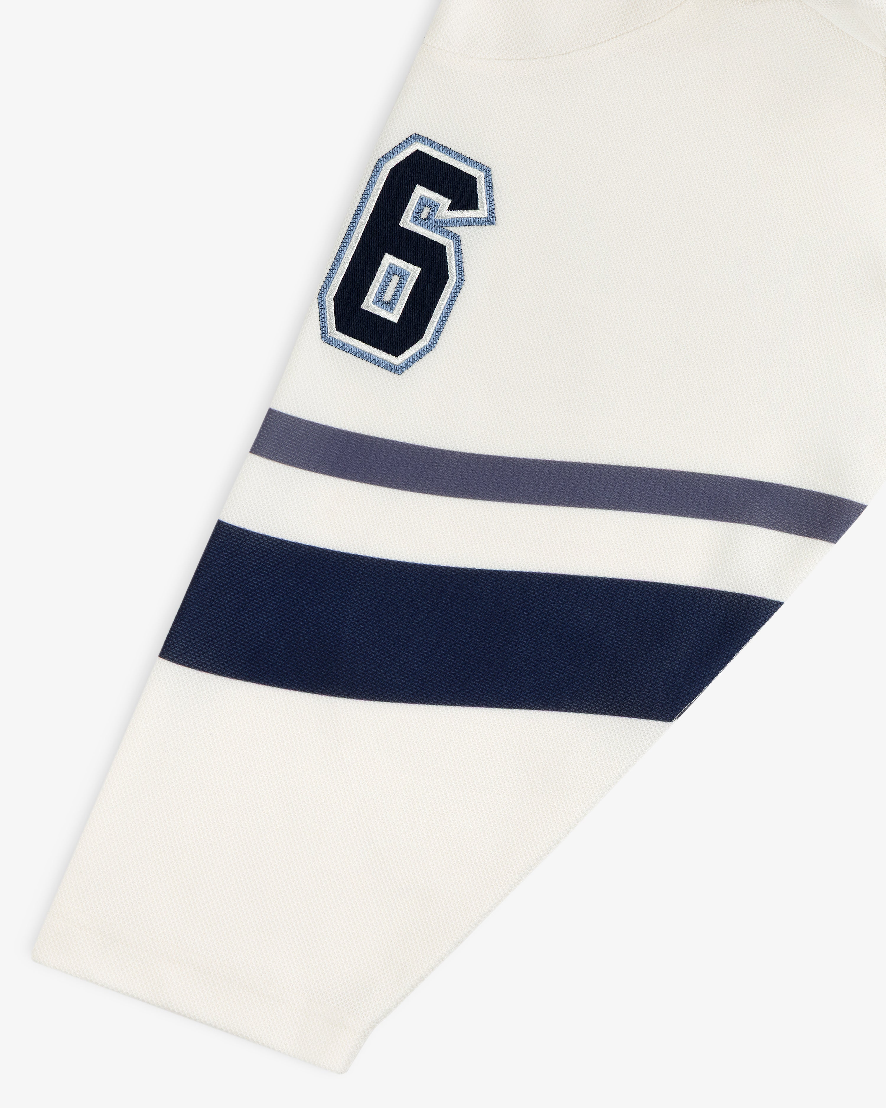 Team Aimé Hockey Jersey sleeve in cream featuring a navy and white number 6 with navy and gray horizontal stripes.
