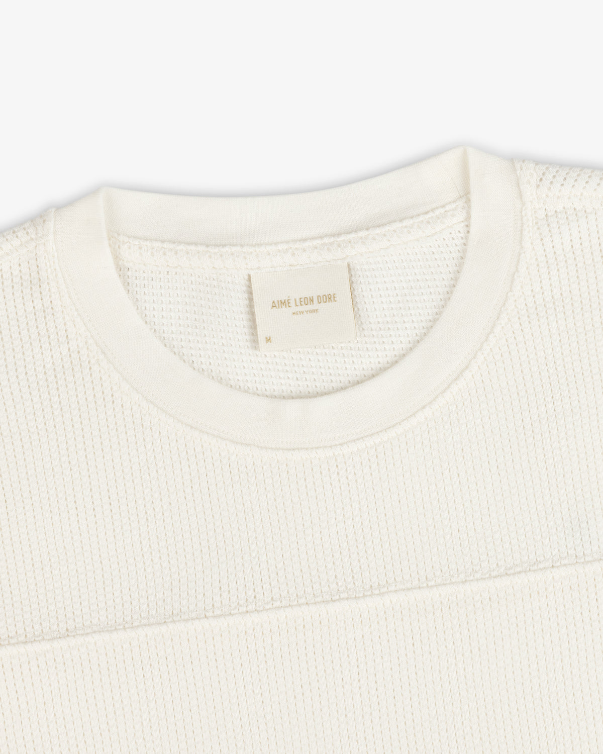 Close-up of a cream Long-Sleeve Mesh Football Tee with a visible Aime Leon Dore label at the collar.