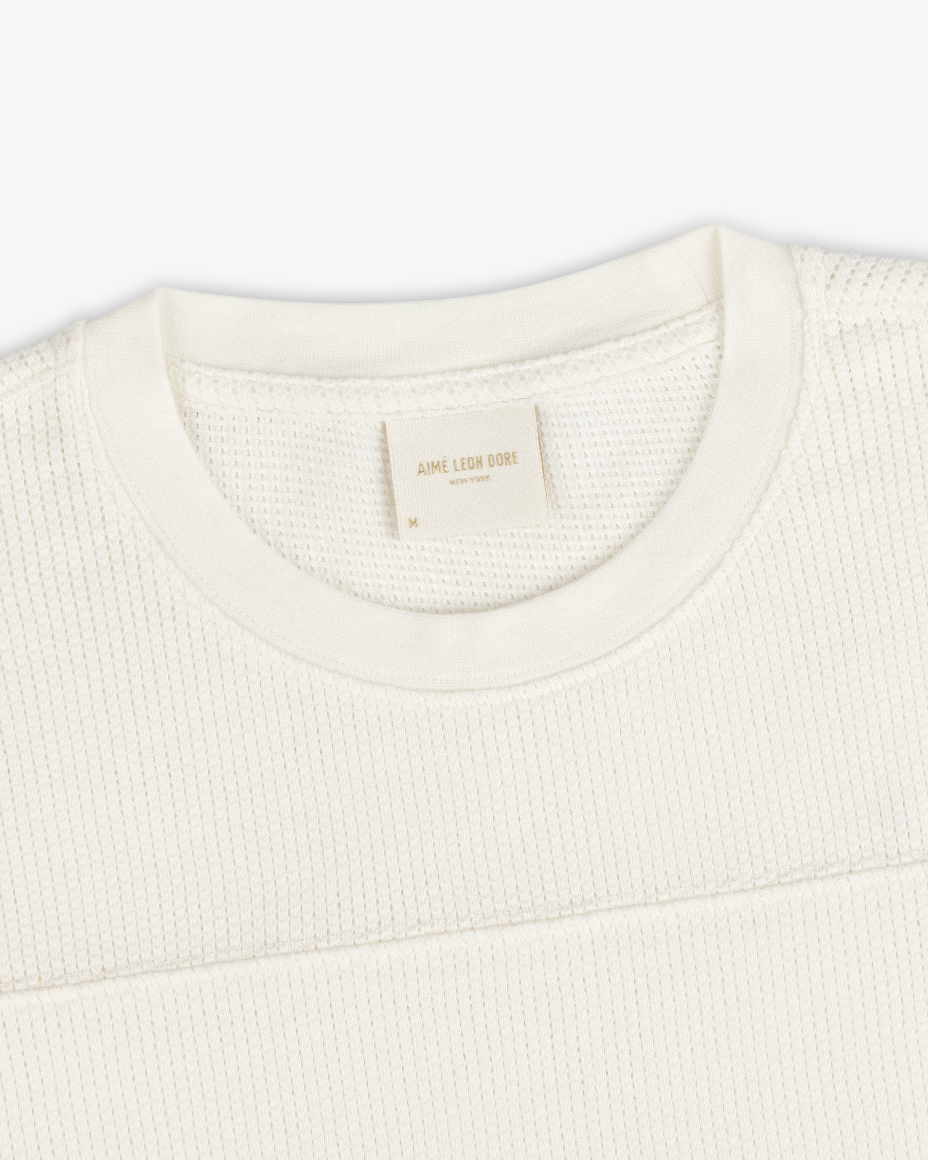 Close-up of a cream Long-Sleeve Mesh Football Tee with a visible Aime Leon Dore label at the collar.