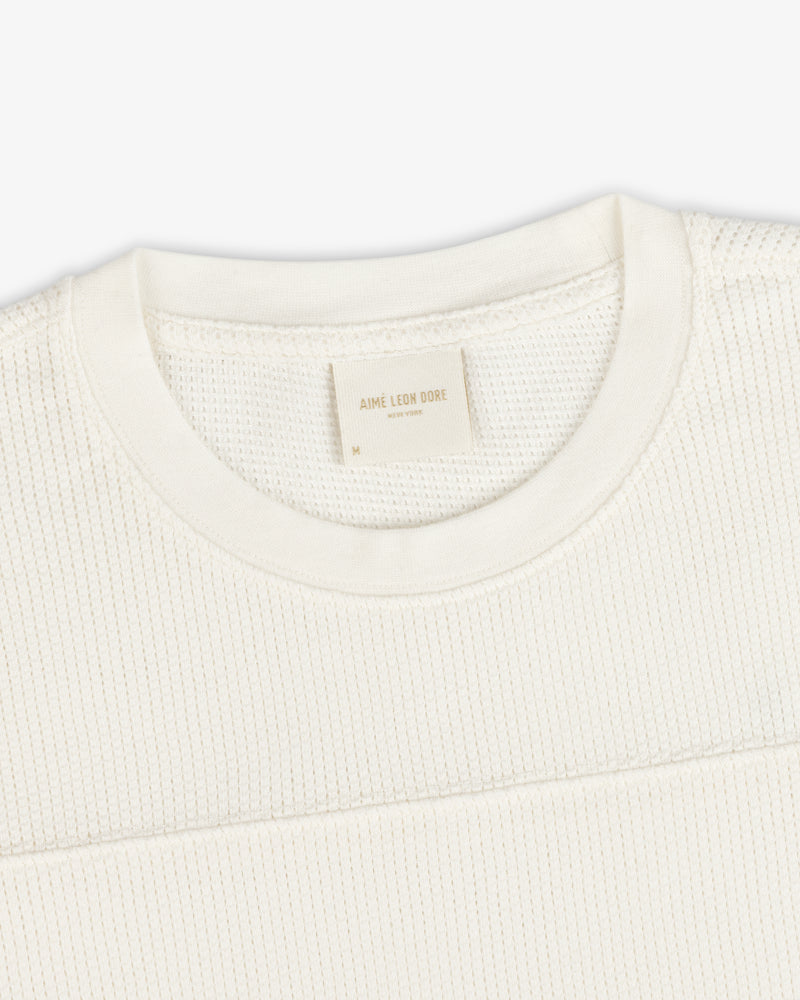Close-up of a cream Long-Sleeve Mesh Football Tee with a visible Aime Leon Dore label at the collar.