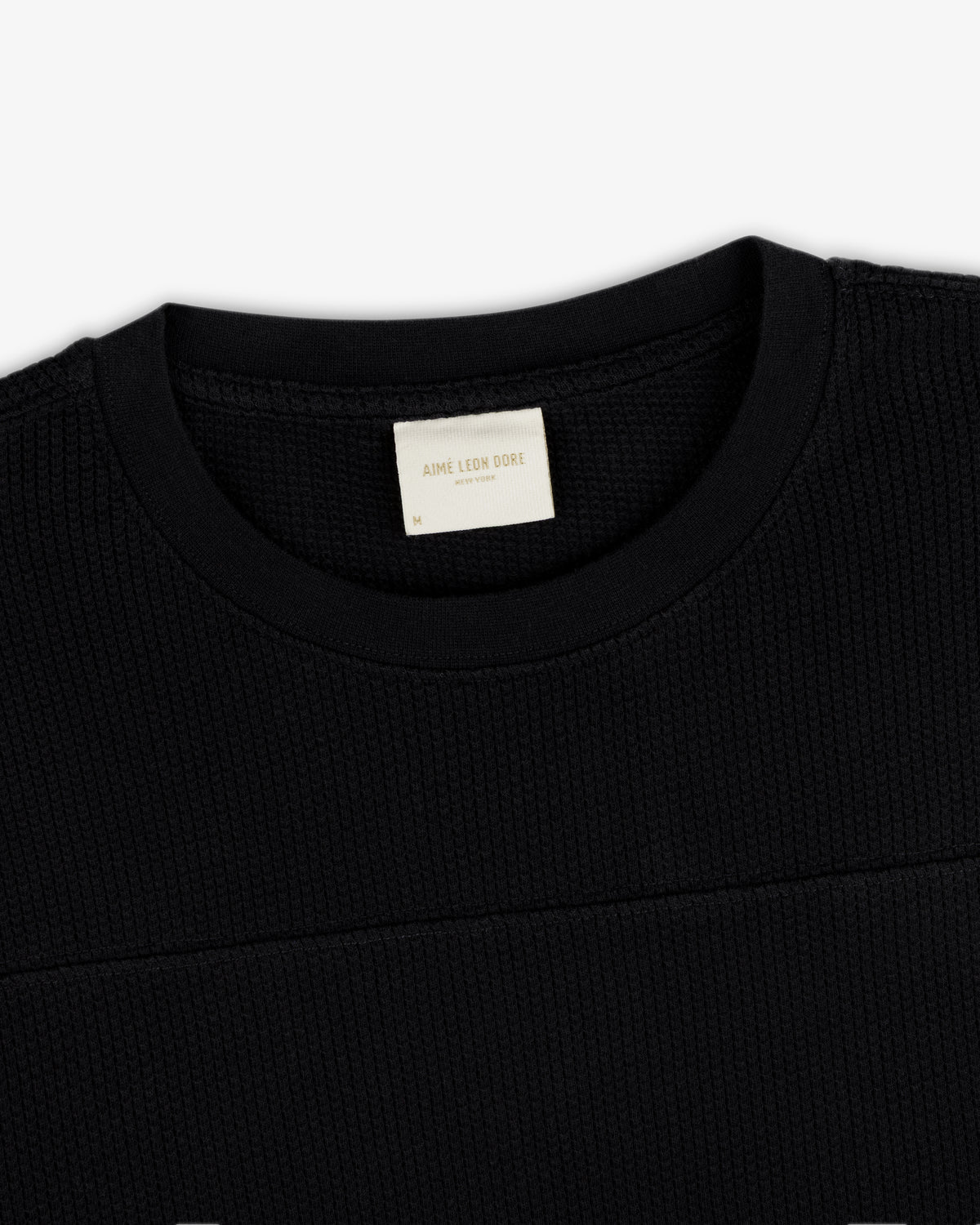 Close-up of a black Long-Sleeve Mesh Football Tee featuring a visible cream Aime Leon Dore label inside the collar.
