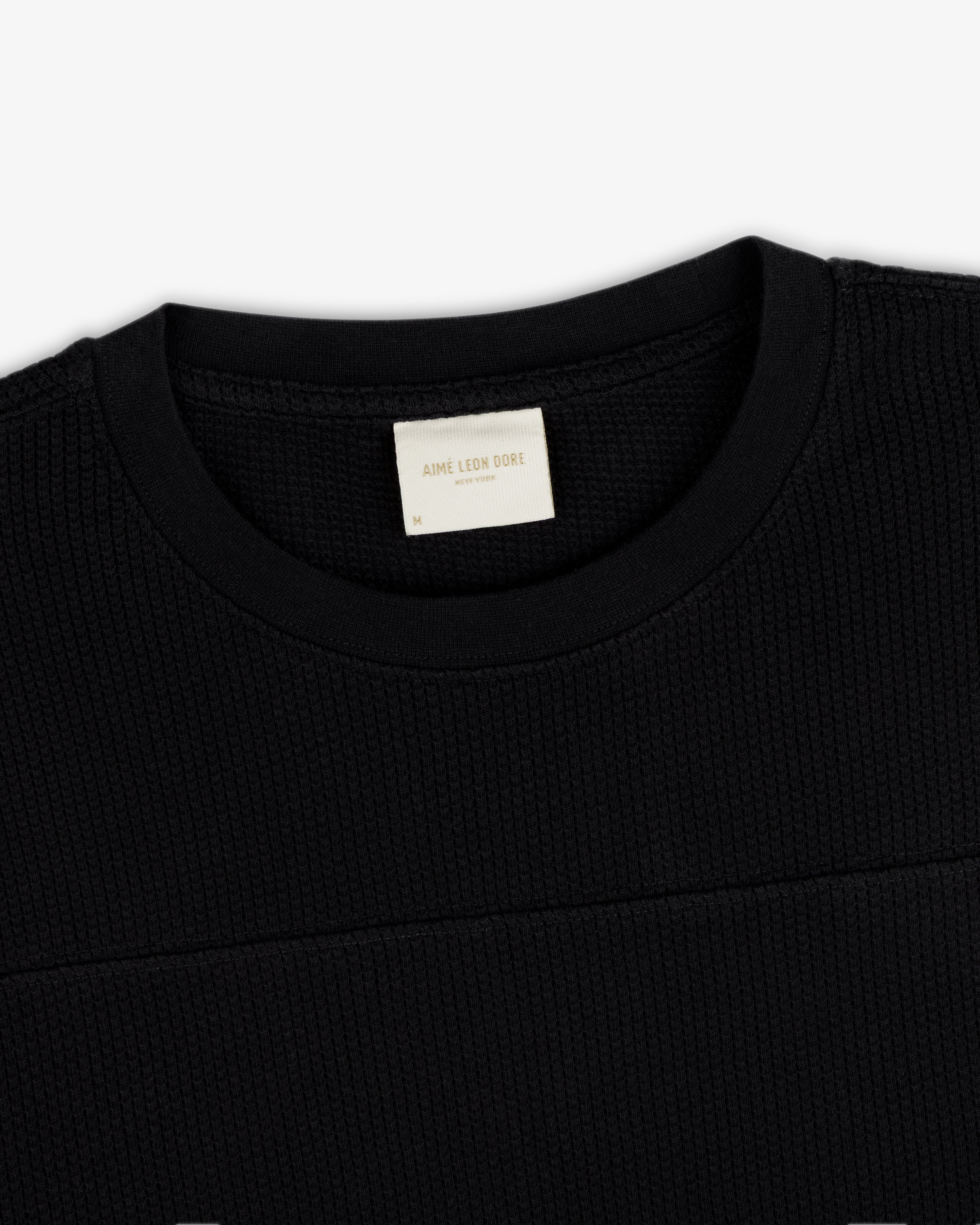 Close-up of a black Long-Sleeve Mesh Football Tee featuring a visible cream Aime Leon Dore label inside the collar.