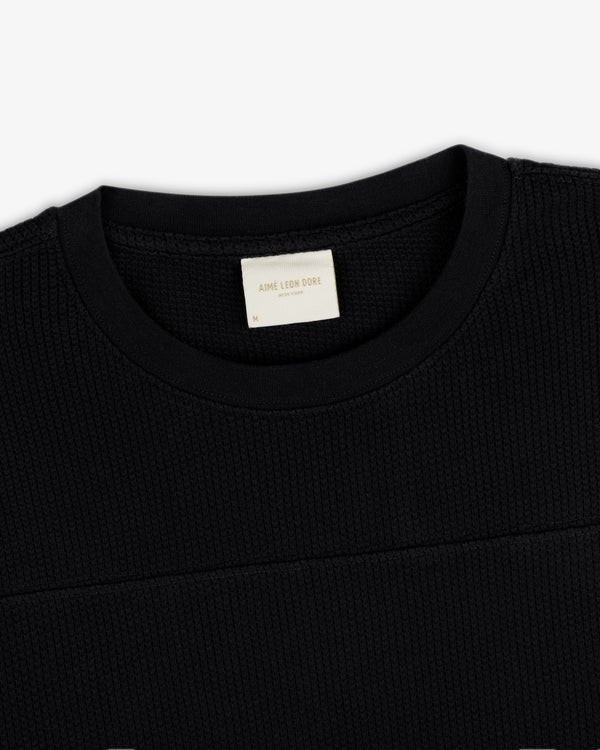 Close-up of a black Long-Sleeve Mesh Football Tee featuring a visible cream Aime Leon Dore label inside the collar.