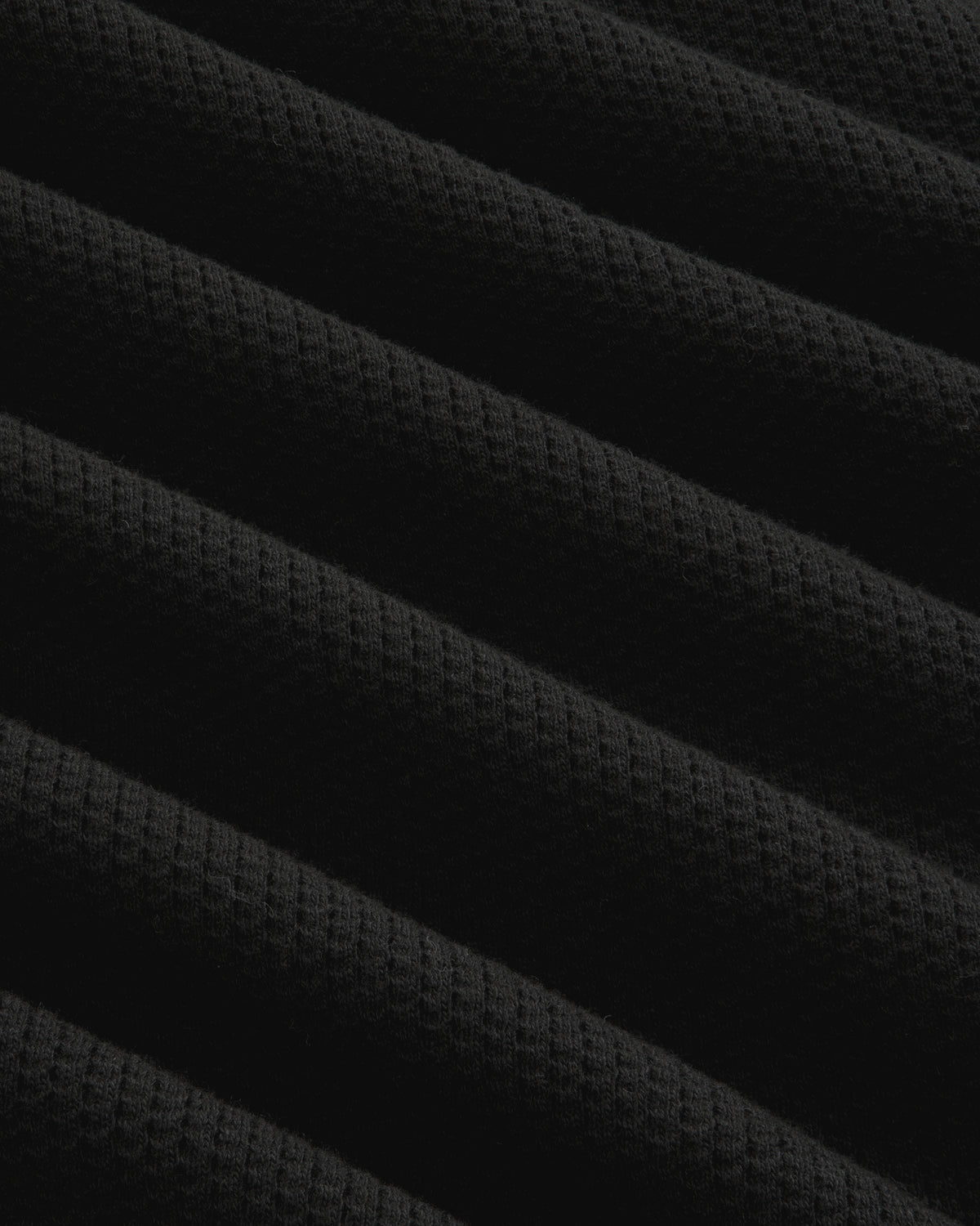 Close-up of Long-Sleeve Mesh Football Tee in black, showing diagonal ridges and waffle texture under soft lighting.