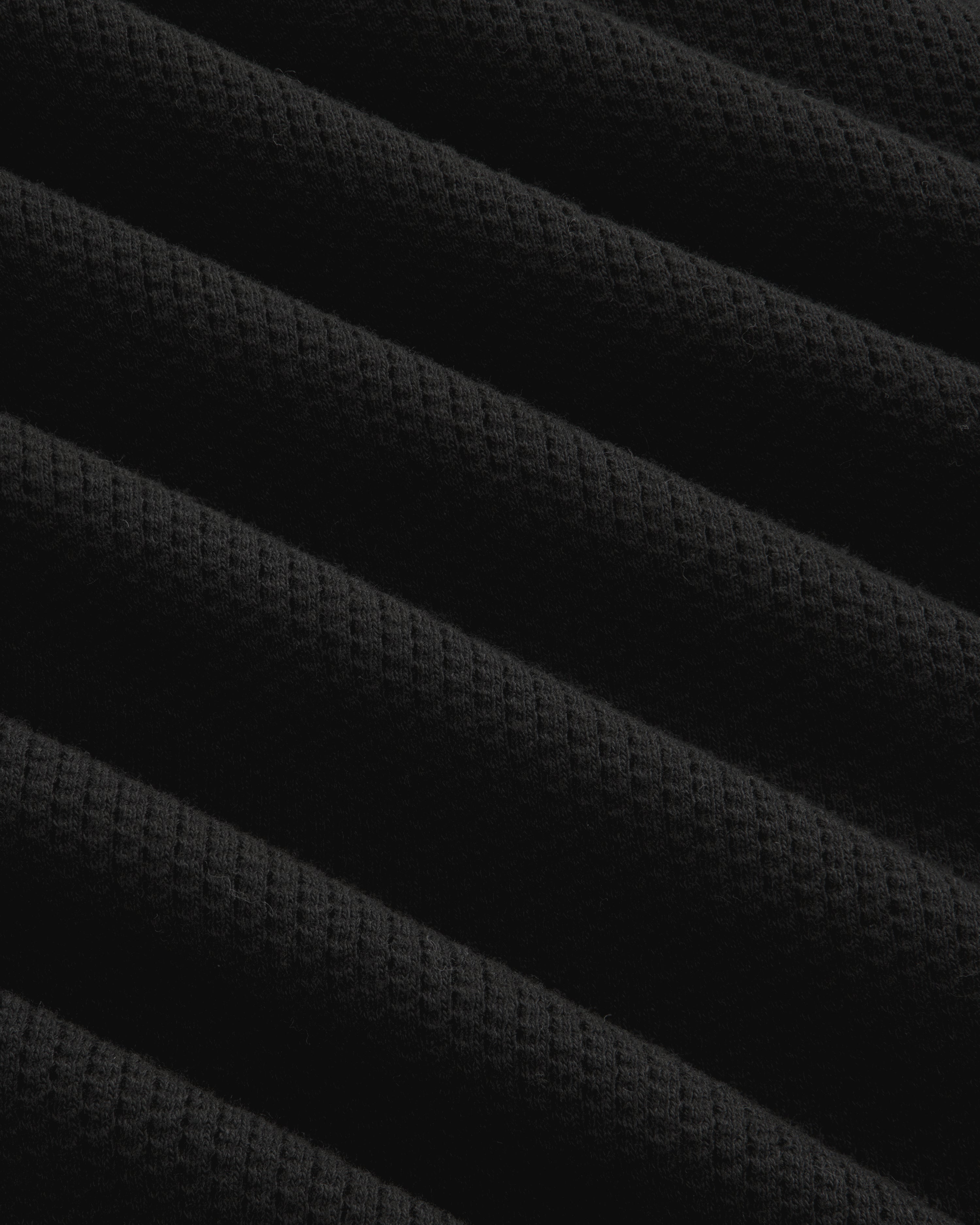 Close-up of Long-Sleeve Mesh Football Tee in black, showing diagonal ridges and waffle texture under soft lighting.