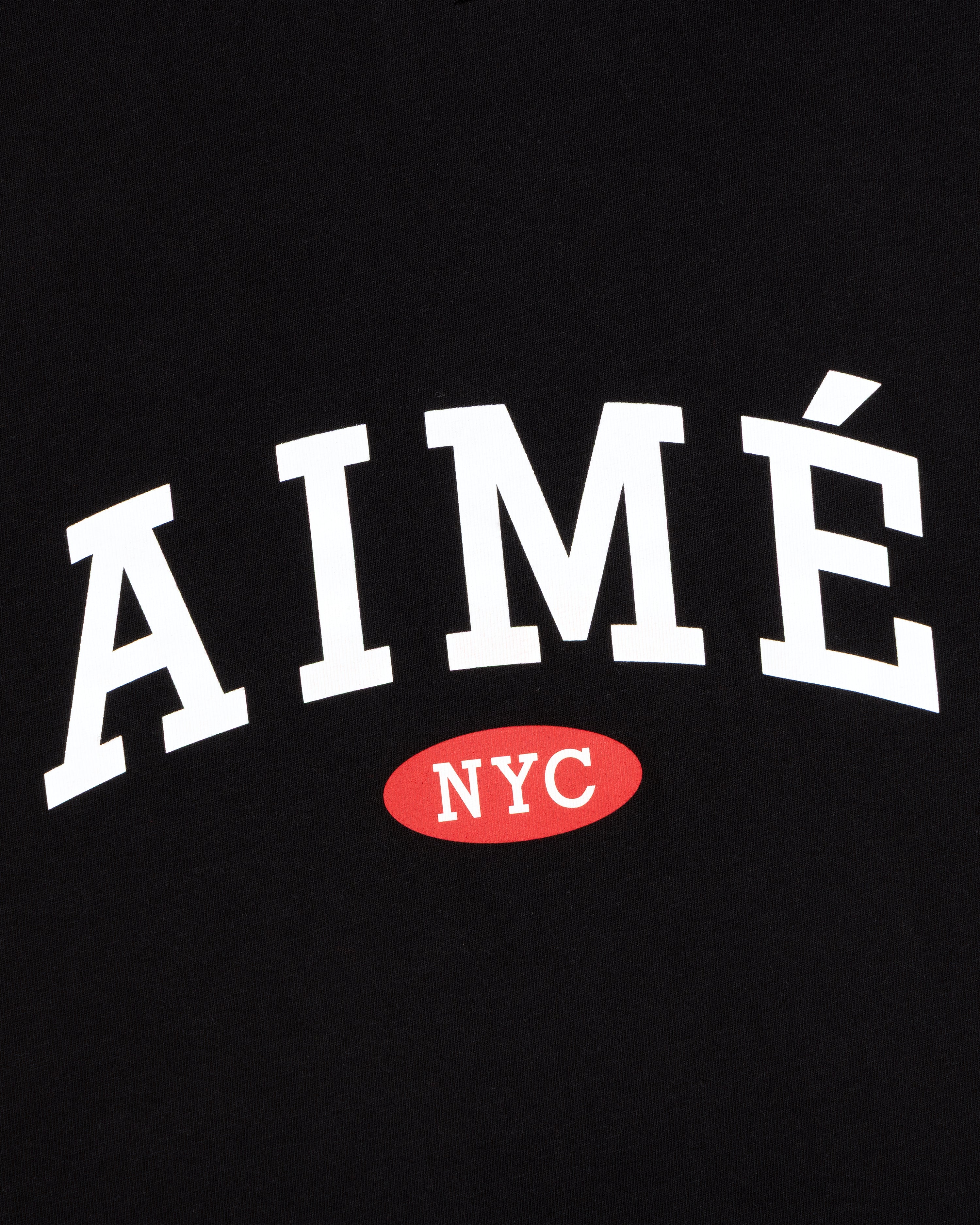 Aimé Souvenir Tee: White AIMÉ text above a red oval with NYC, set on a black background.