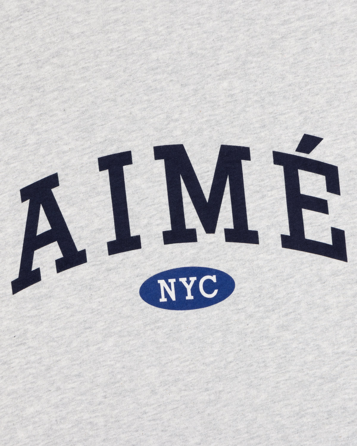 Gray Aimé Souvenir Tee with bold black AIMÉ, and NYC in white inside a blue oval underneath.