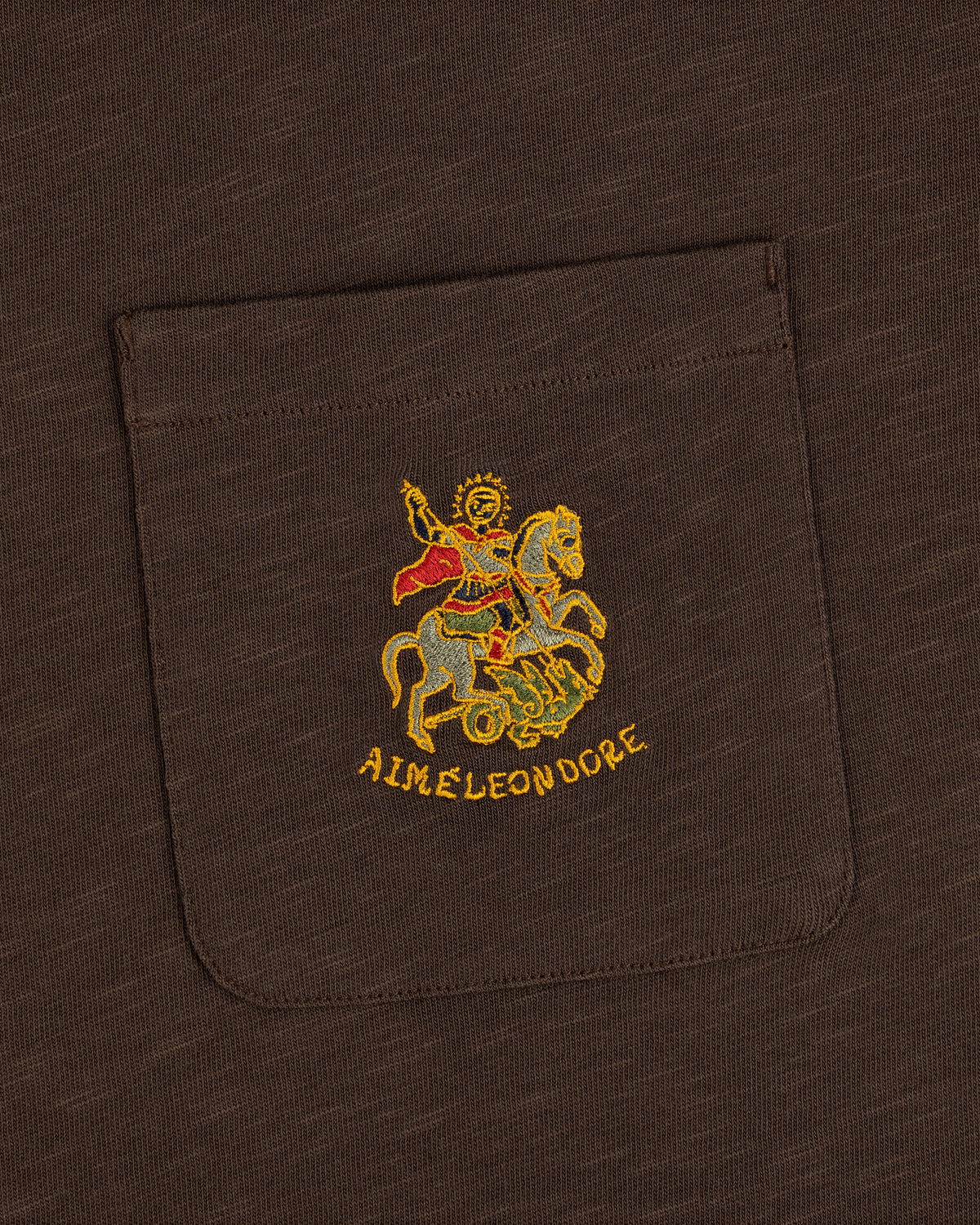 Saint George Slub Pocket Tee: brown pocket tee with gold horse figure embroidery and AIMÉ LEON DORE text below.