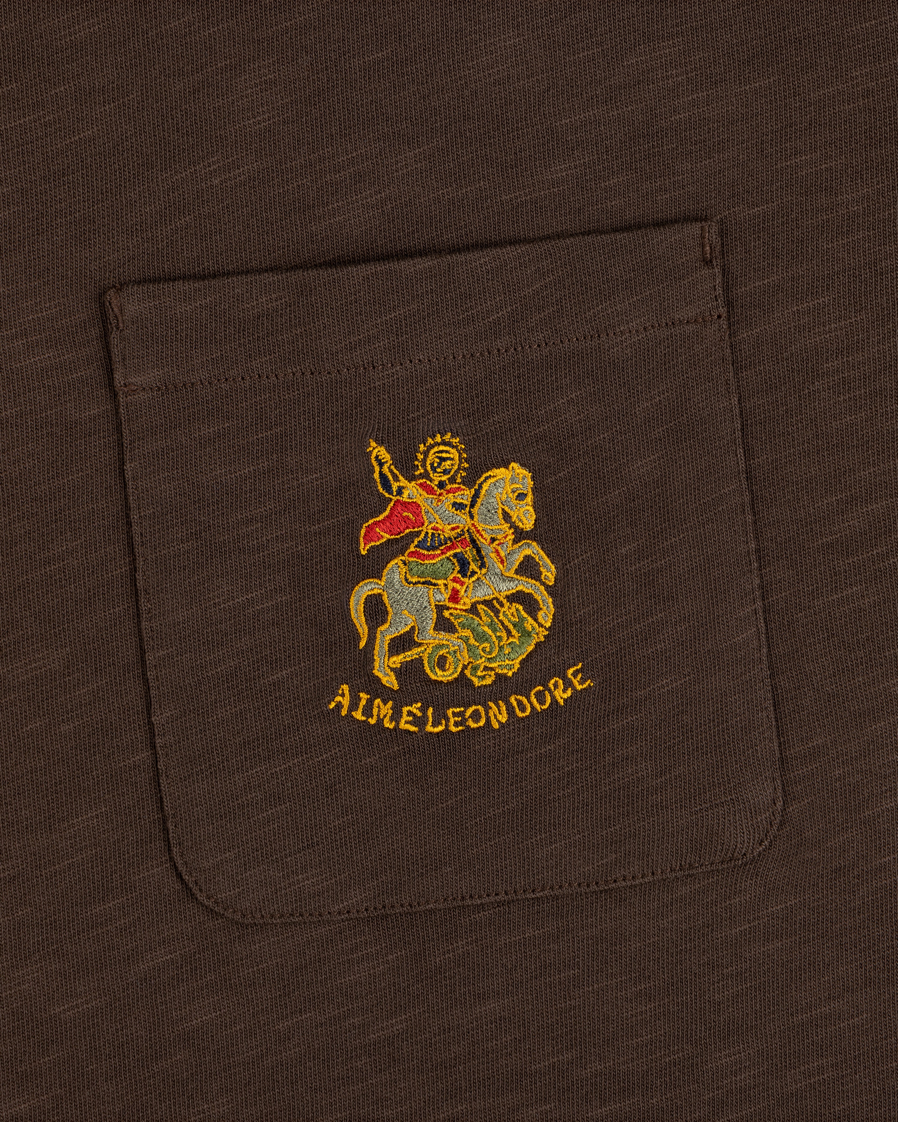 Saint George Slub Pocket Tee: brown pocket tee with gold horse figure embroidery and AIMÉ LEON DORE text below.