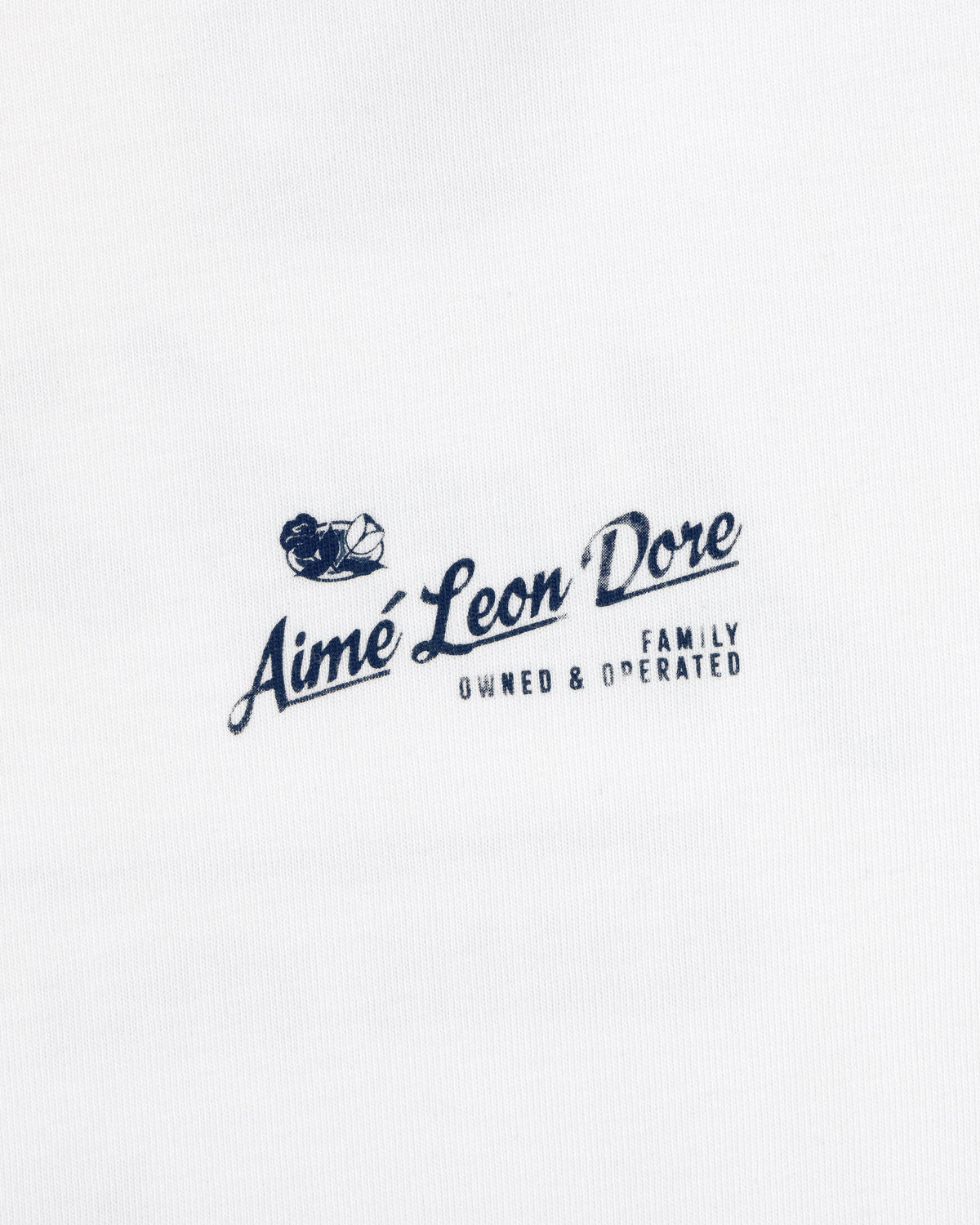 White Neighborhood Tee with a navy Aimé Leon Dore Family Owned & Operated logo and sailing boat graphic above the text.