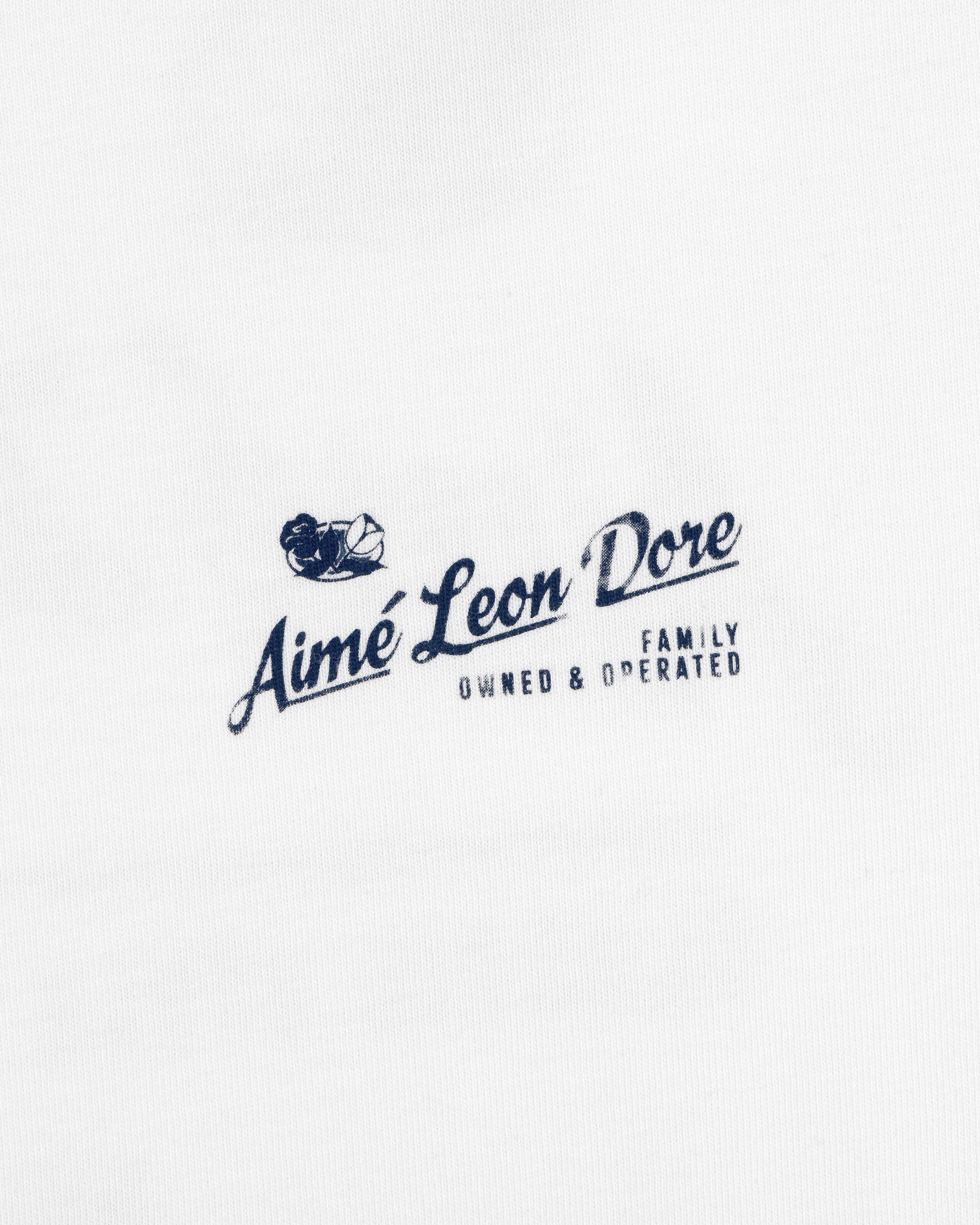 White Neighborhood Tee with a navy Aimé Leon Dore Family Owned & Operated logo and sailing boat graphic above the text.