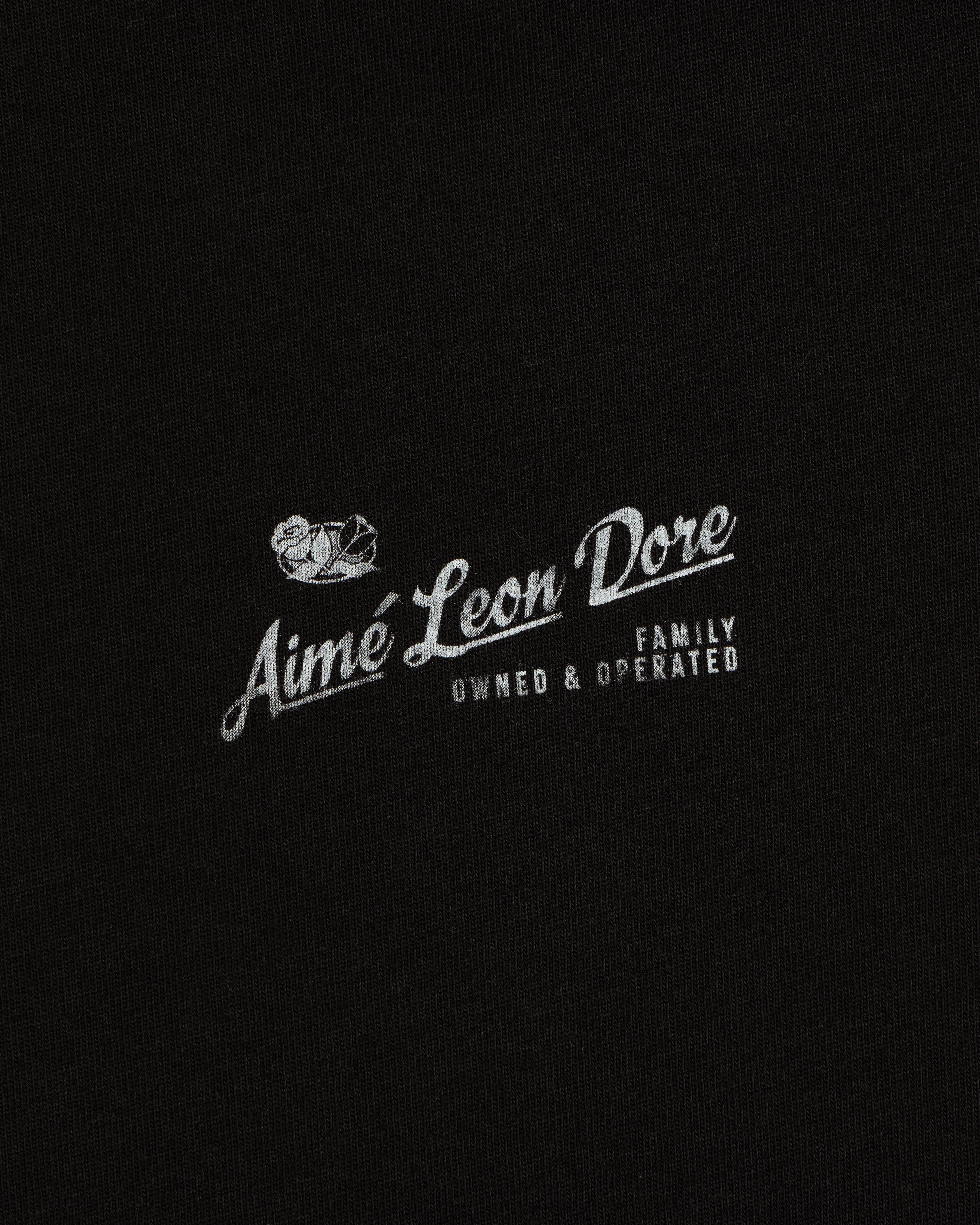 Neighborhood Tee featuring white “Aime Leon Dore Family Owned & Operated” text and duck logo on black fabric.