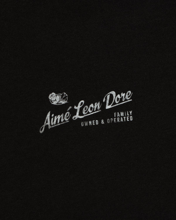 Neighborhood Tee featuring white “Aime Leon Dore Family Owned & Operated” text and duck logo on black fabric.