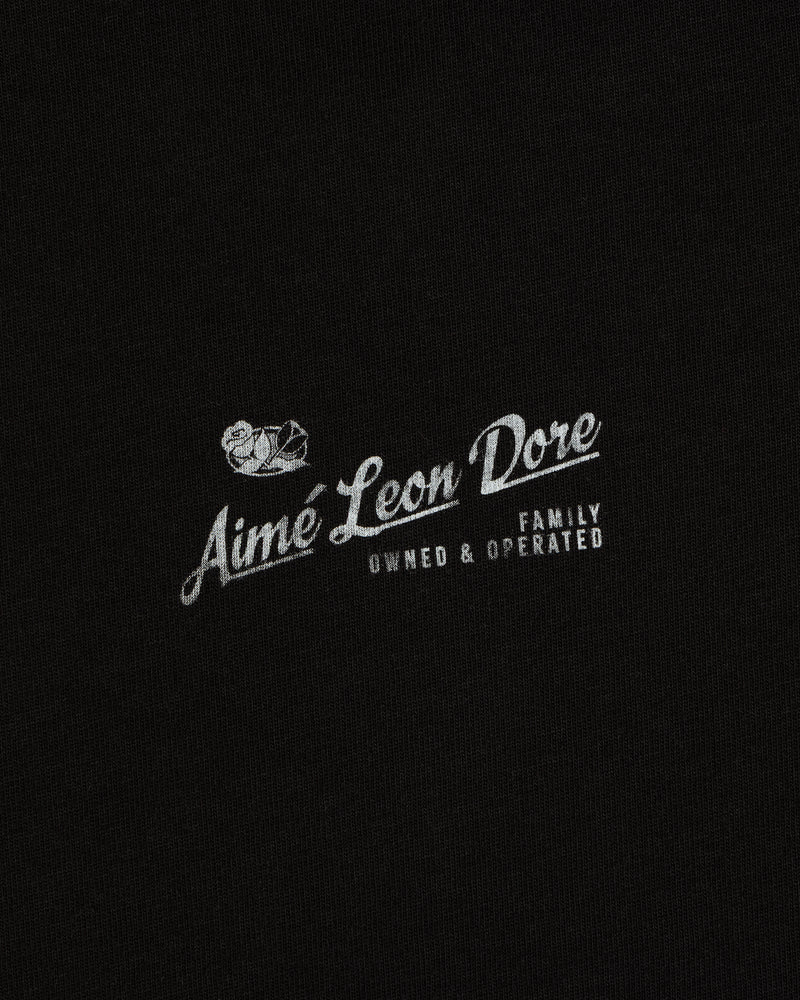 Neighborhood Tee featuring white “Aime Leon Dore Family Owned & Operated” text and duck logo on black fabric.