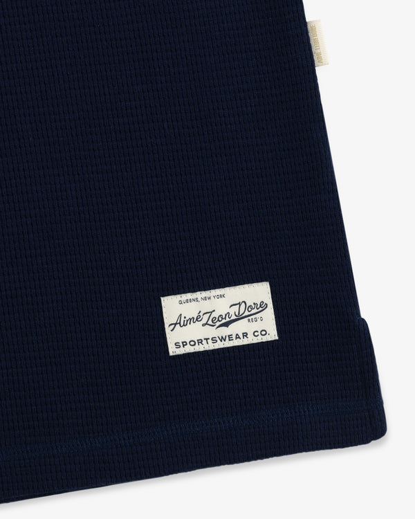 Dark blue waffle-knit Long-Sleeve Waffle Henley with a rectangular brand patch featuring cursive text.